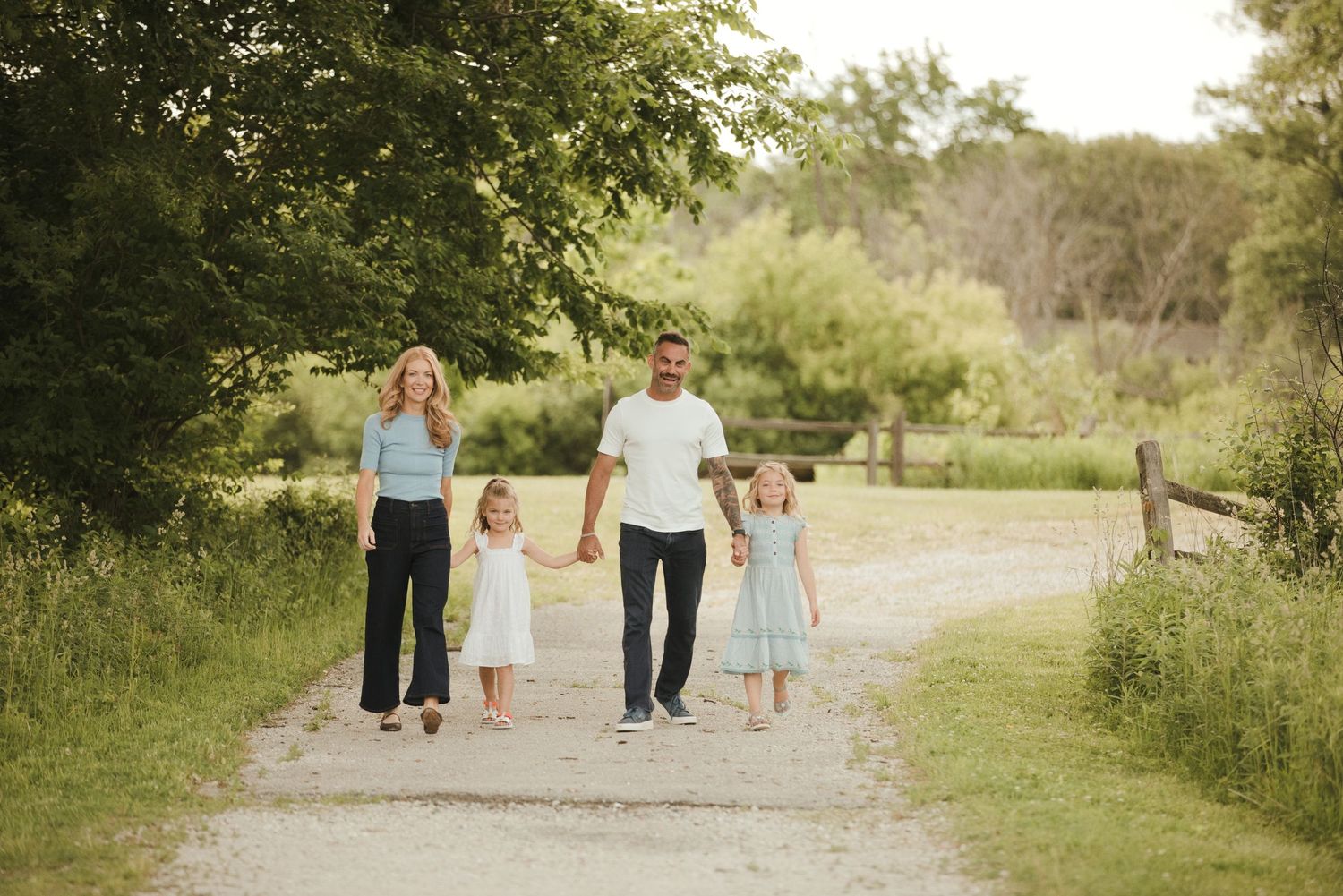 Family of four walking hand-in-hand on a scenic gravel path surrounded by lush greenery.