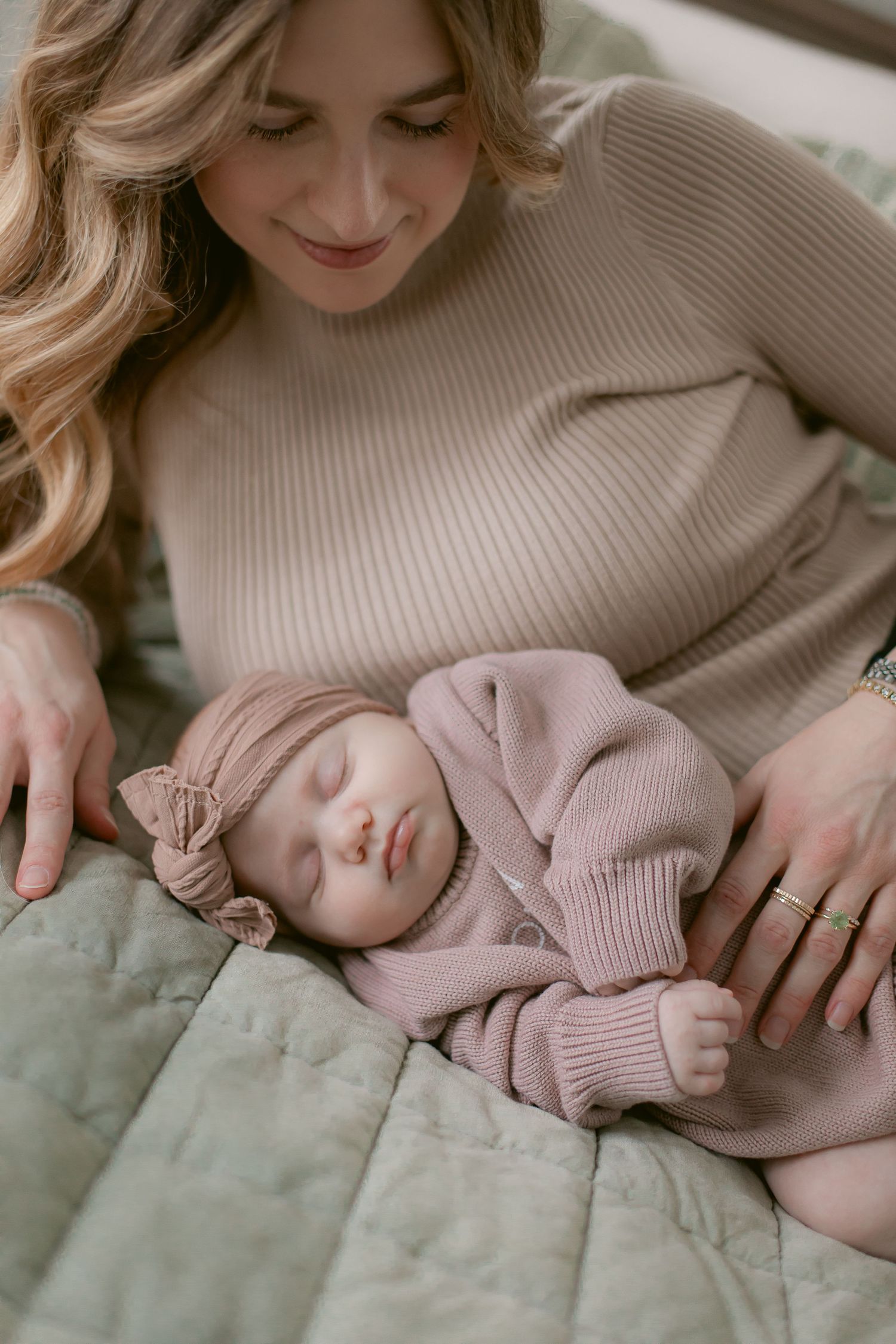 Infant wearing soft pink sweater sleeping peacefully on quilted bedding.