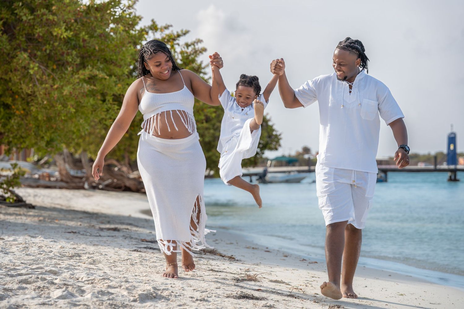A group in white outfits walking along a tropical beach with turquoise waters in the background.