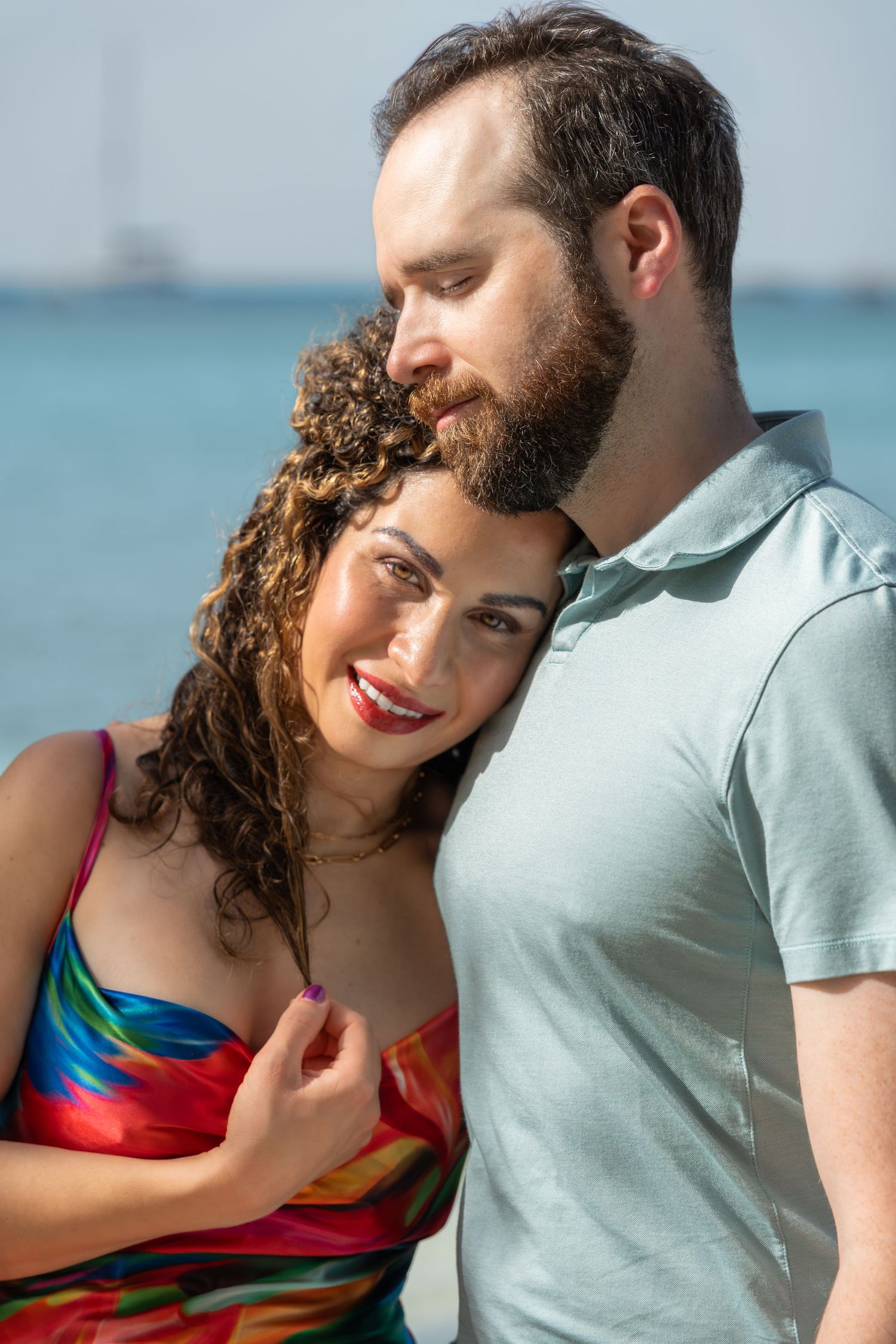 Romantic couple embracing by the ocean wearing colorful summer attire.