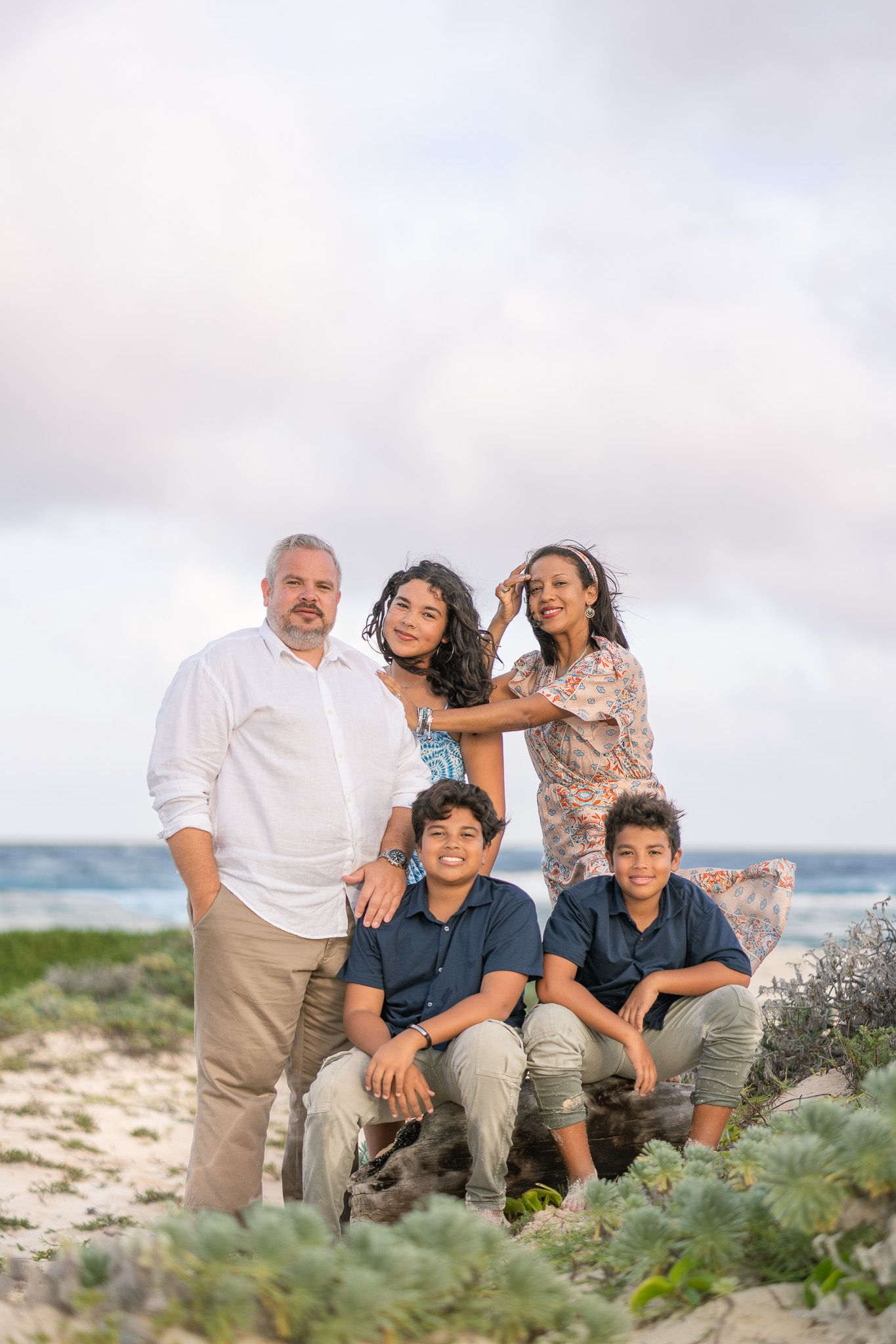 Group portrait of a family sitting together on a sandy beach with vegetation.