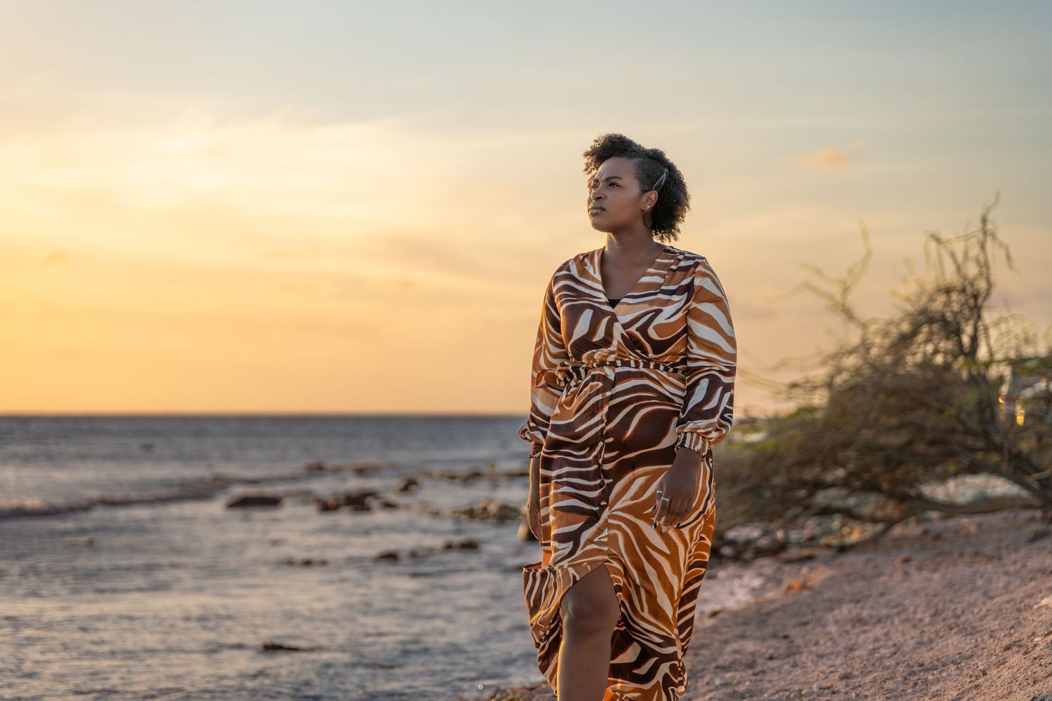 Person in zebra print dress poses against sunset backdrop near lighthouse.