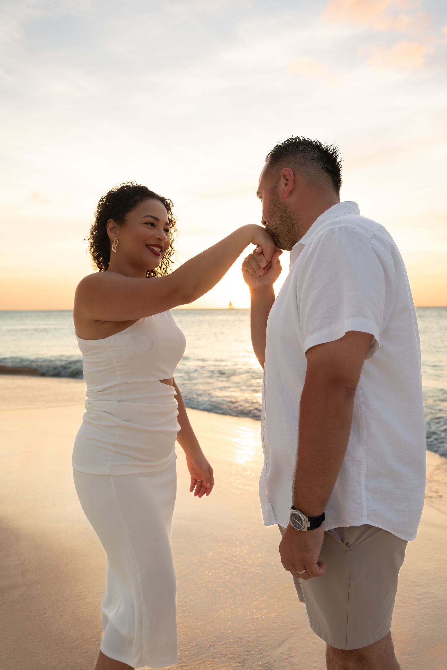 Romantic beach moment between couple in white attire during sunset.