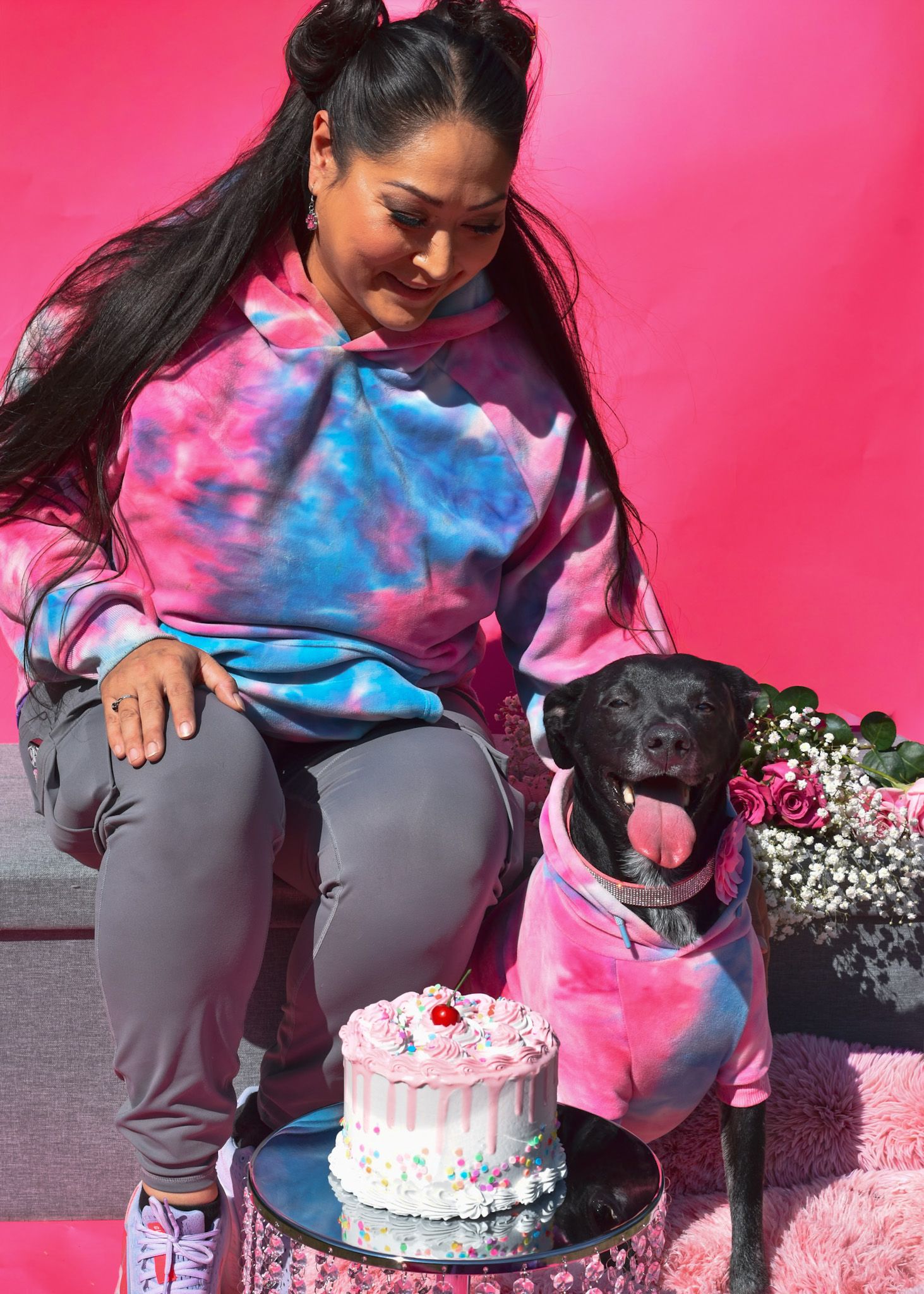 Dog and owner celebrate with decorated birthday cake against pink backdrop.