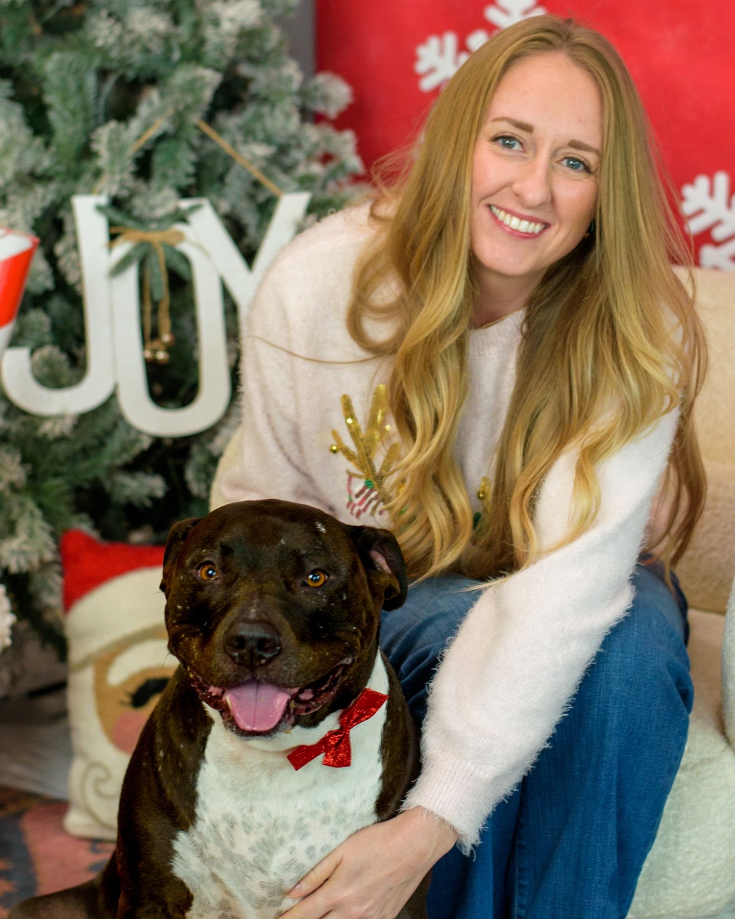 Dog and companion posing for holiday photos with Christmas decorations.