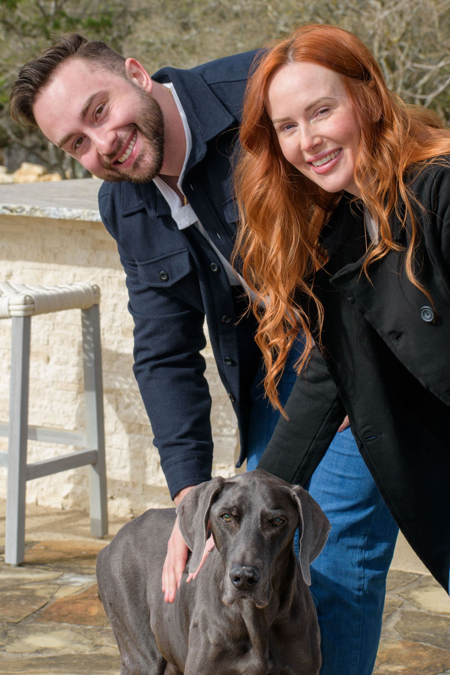 Grey Great Dane posing for photos with its owners outdoors.