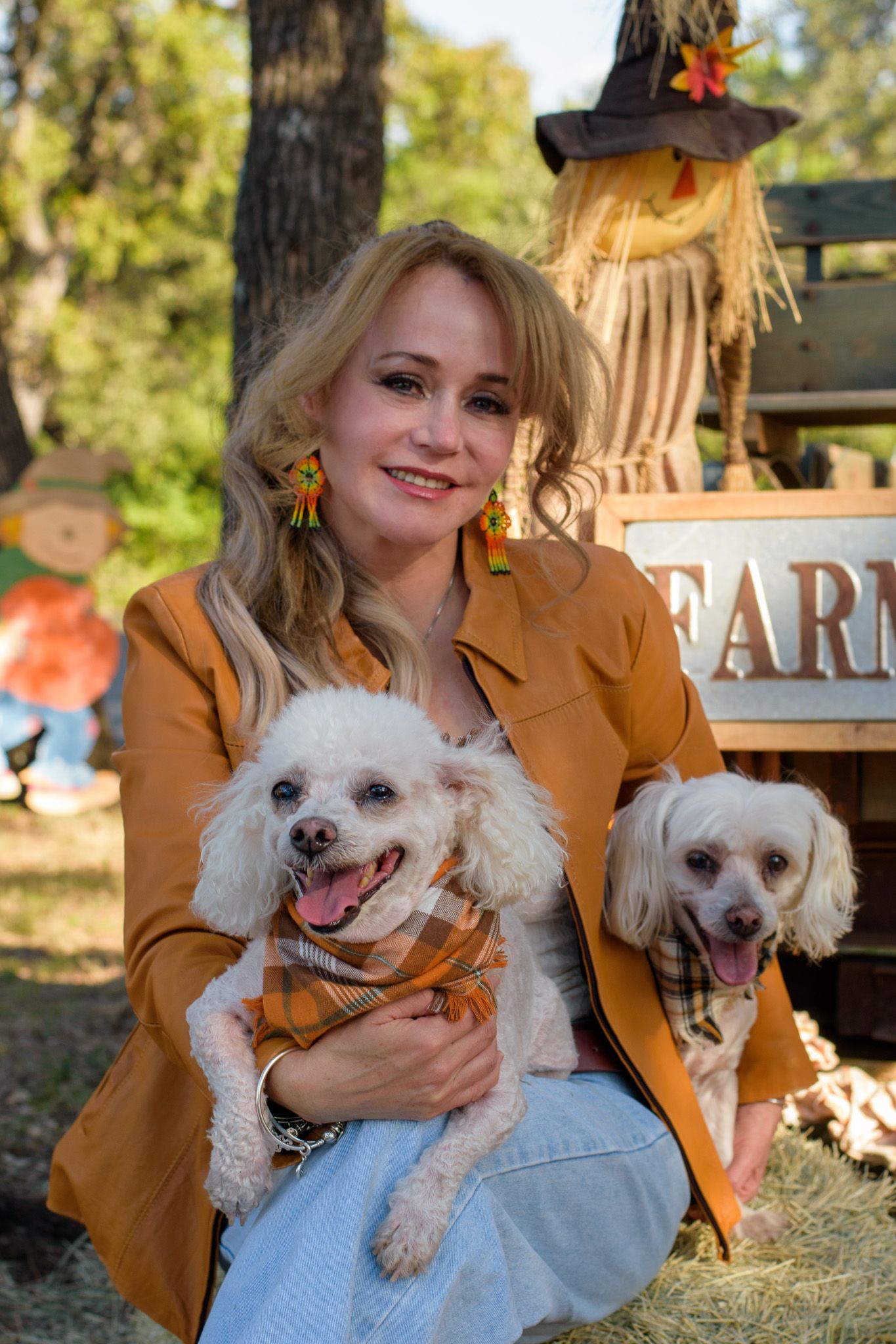 Person in yellow jacket holds two small white dogs outdoors during autumn.