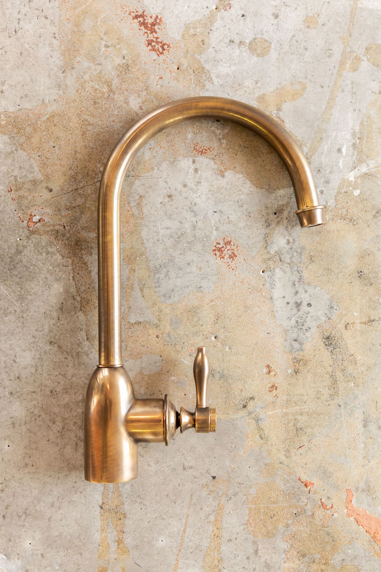 An antique brass kitchen faucet mounted on a weathered stone wall background.