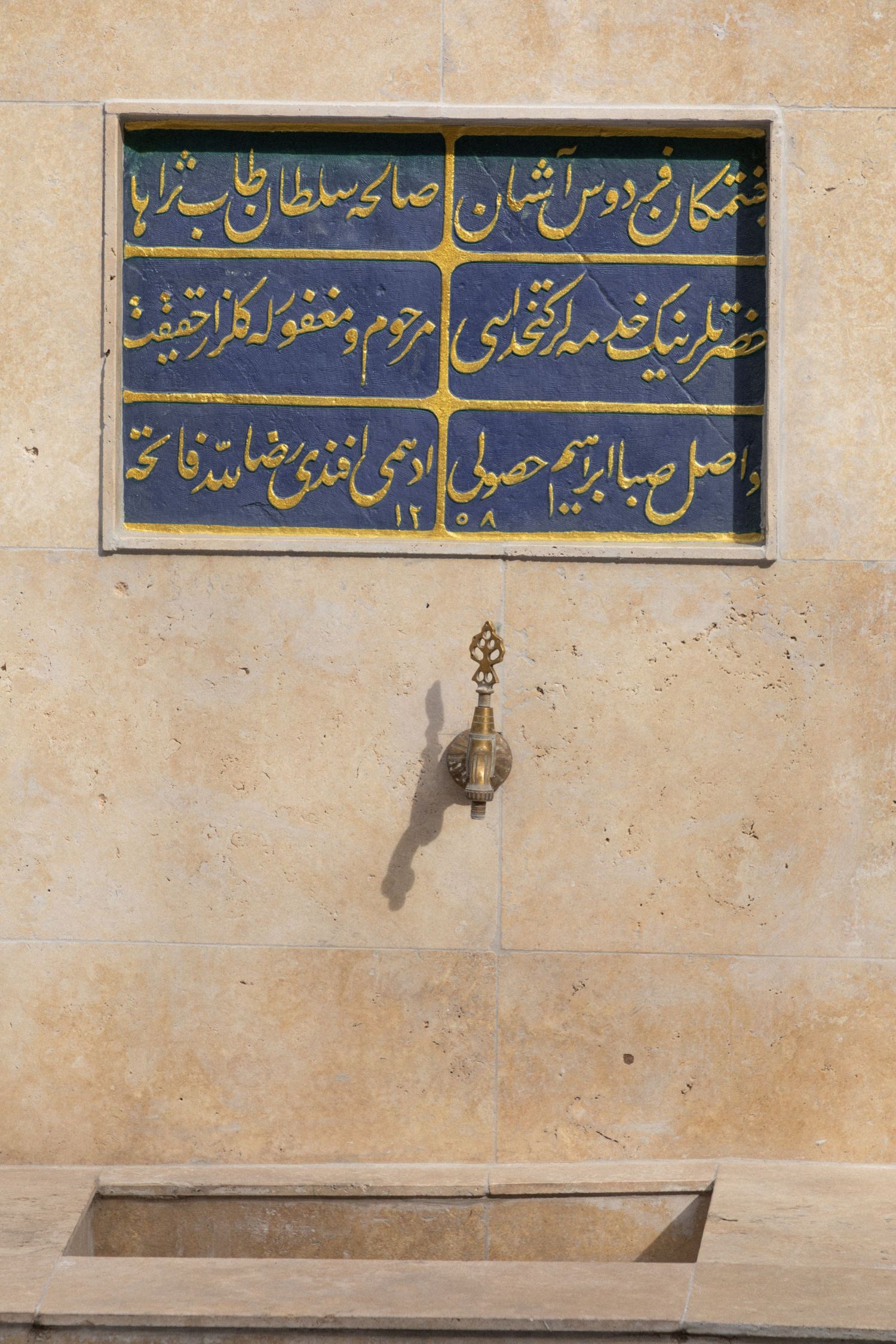 Ottoman Turkish calligraphy inscription on decorative tiles above a brass water fountain spout.