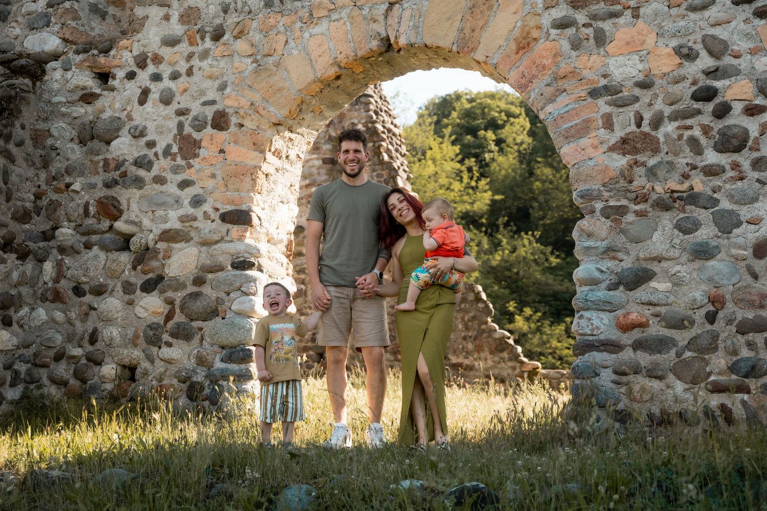 Family of four standing together inside a rustic stone archway of historic ruins in warm golden light.