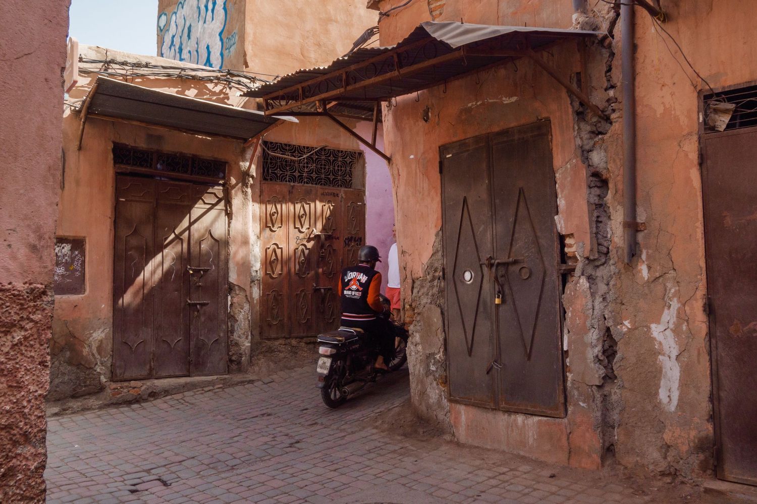 Delivery rider on a scooter navigating a narrow alley in the Marrakech medina, Morocco.