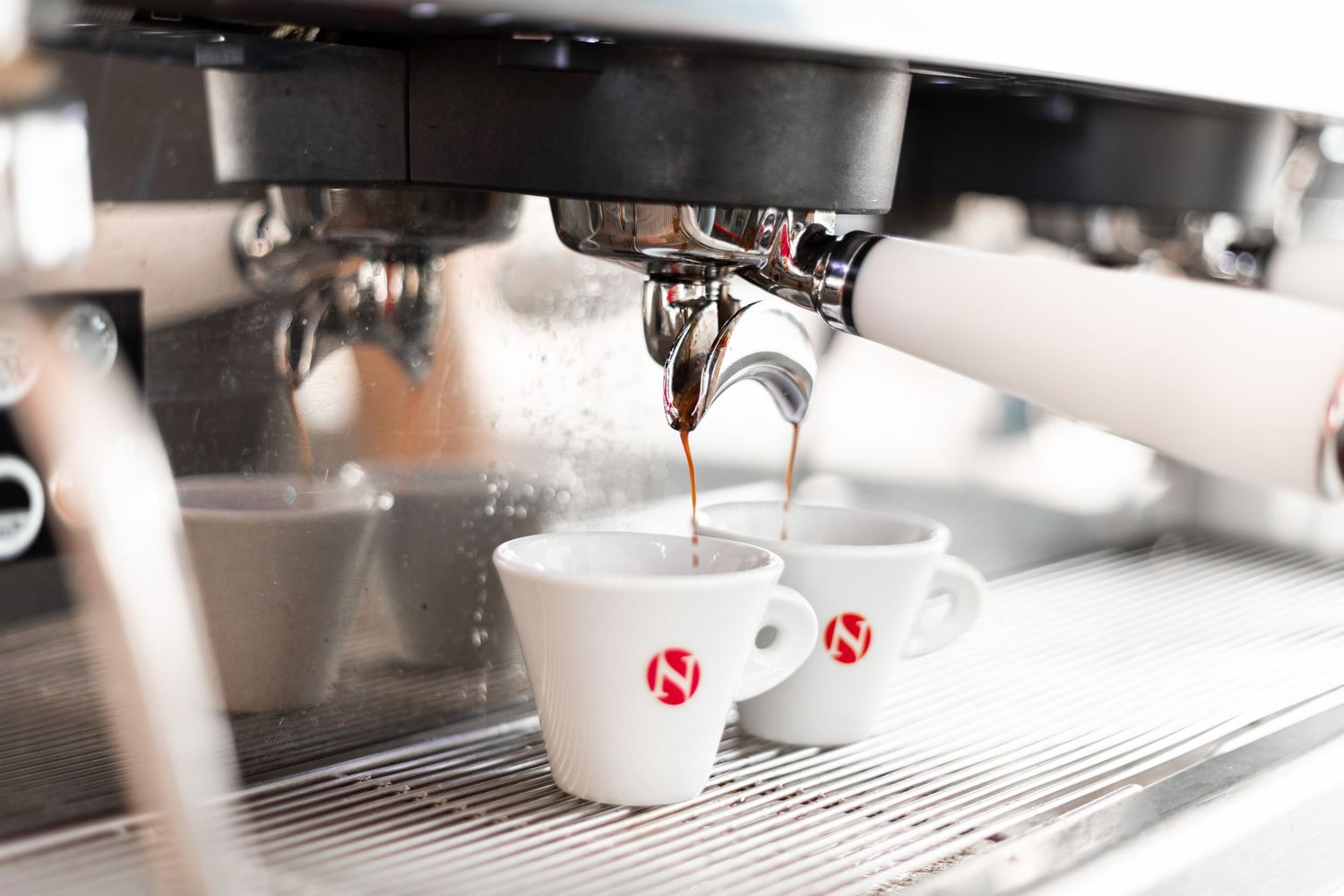 Espresso machine brewing fresh coffee into two white branded cups simultaneously.