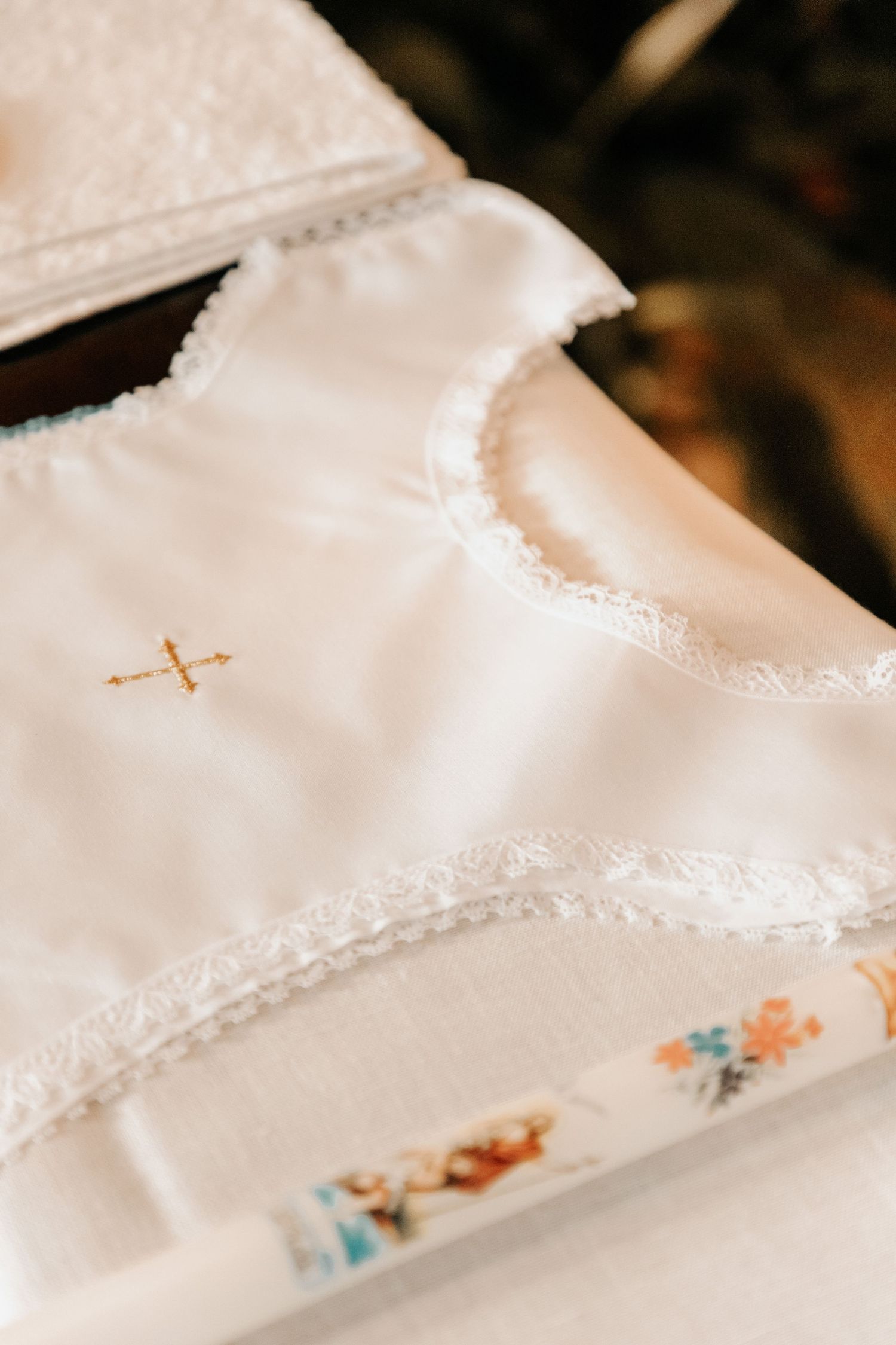 White baptism gown with gold cross embroidery and delicate lace trim laid flat on a white surface.