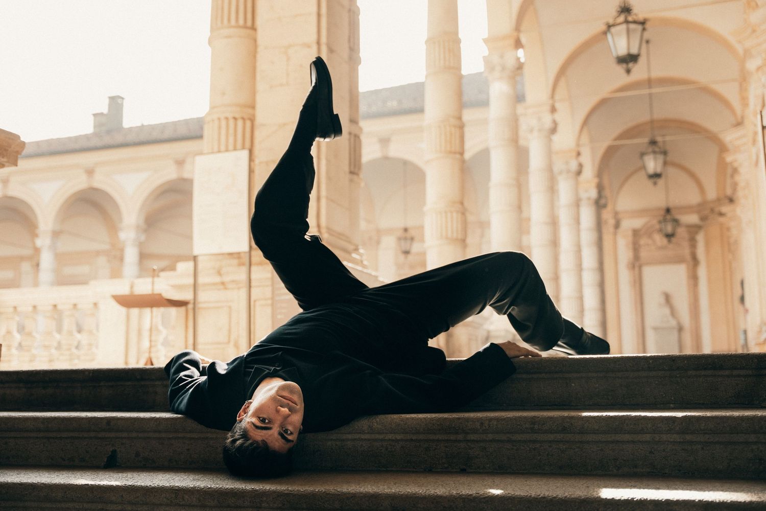 Male dancer in black performing acrobatic move on steps of elegant classical building.