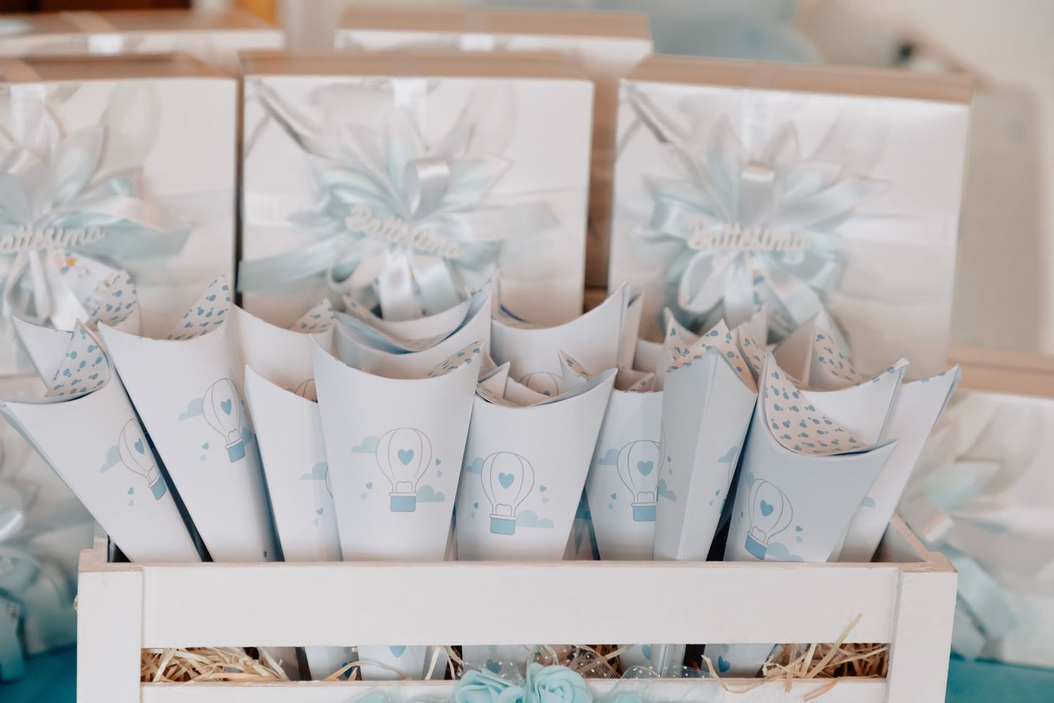 Decorative baby shower favor cones with blue and white designs arranged in a wooden crate with straw.