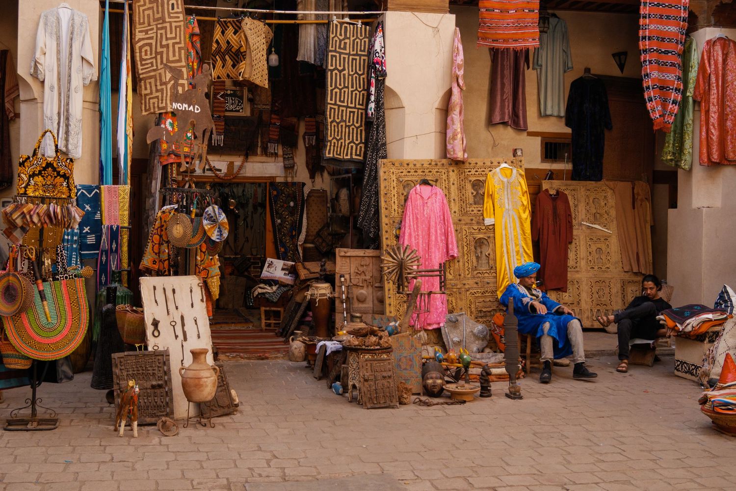 Colorful Moroccan market stall displaying traditional textiles, crafts, and woven baskets in the medina.