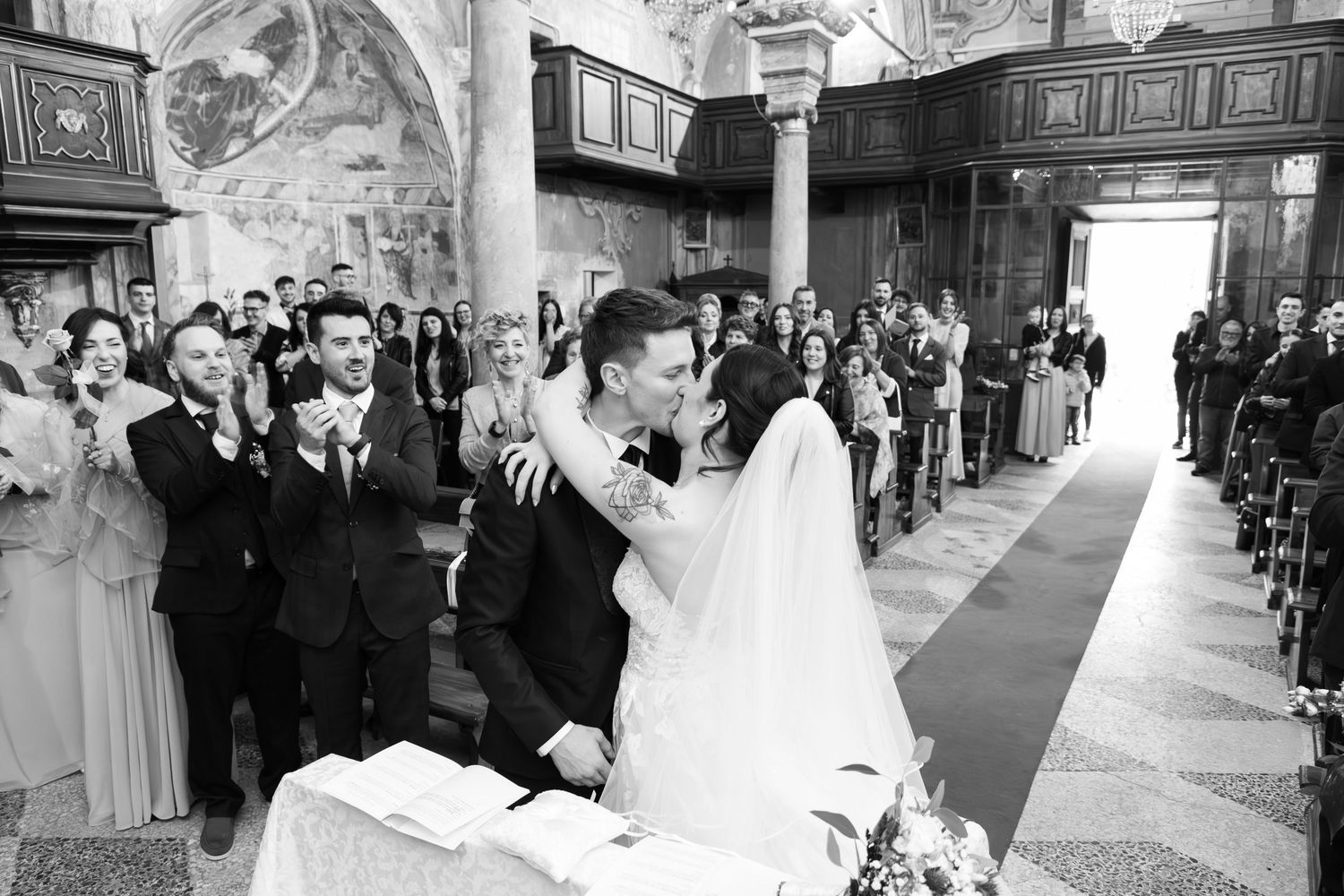 Bride and groom share first kiss at church altar in black and white wedding photo.