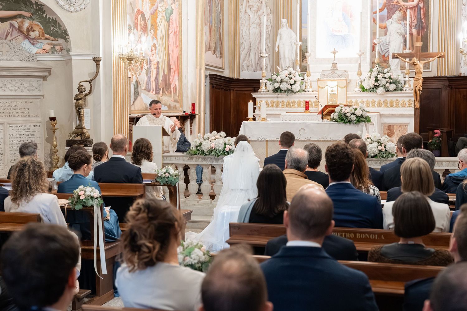 Priest officiates wedding ceremony at ornate church altar with seated guests.