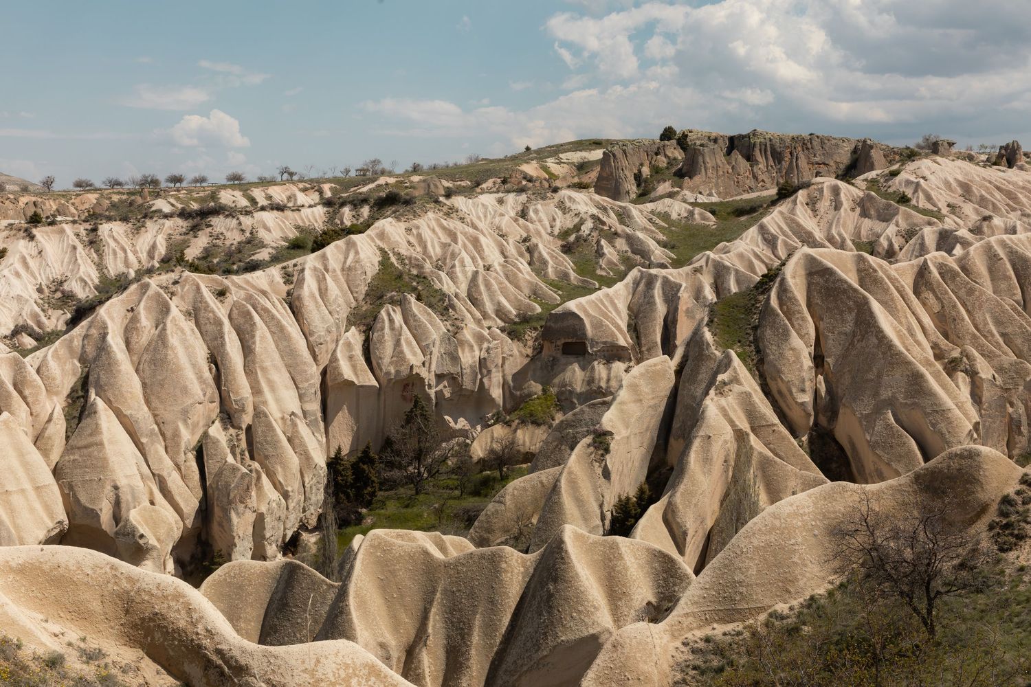 Dramatic eroded rock formations and valleys in Cappadocia, Turkey, under a partly cloudy sky.