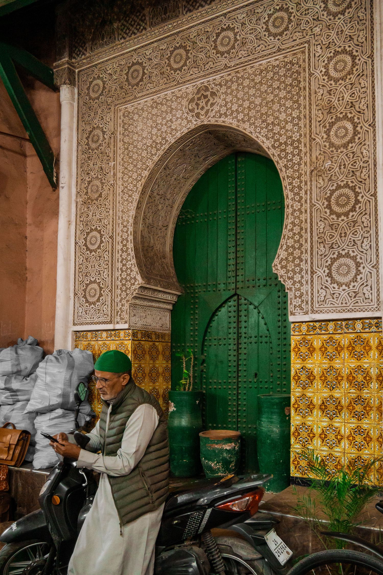 Elderly man standing beside an ornate green Moorish archway with decorative tilework in Marrakech.