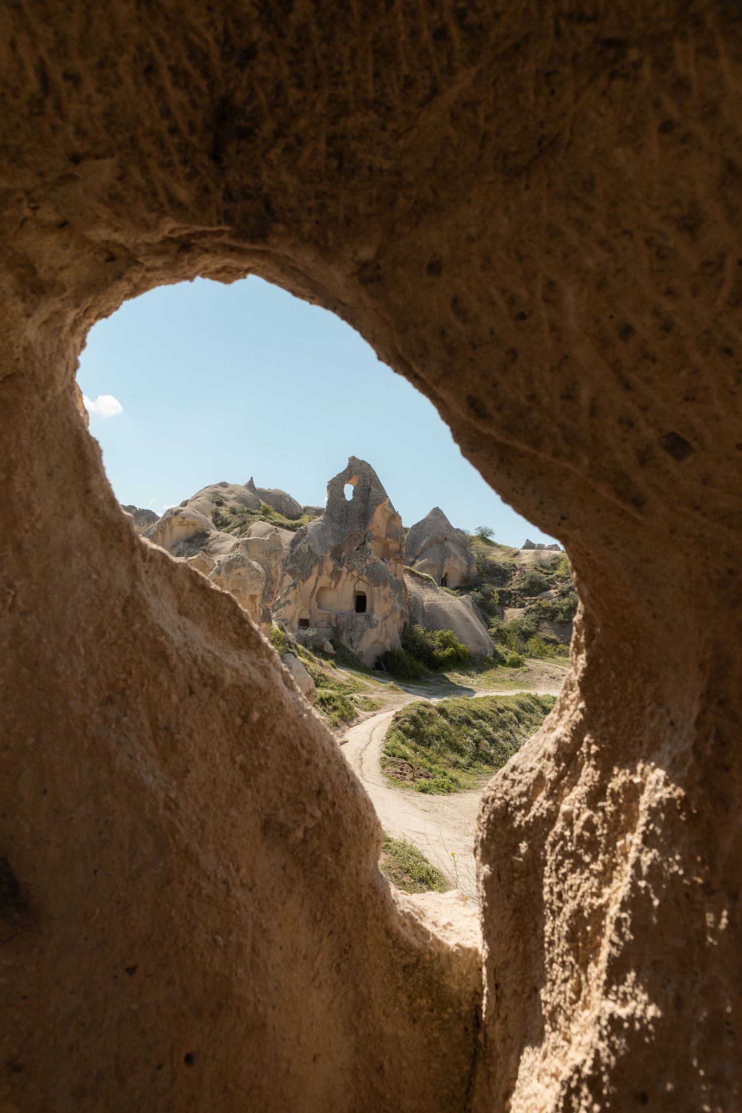 Oval cave opening framing a view of ancient rock-cut dwellings and fairy chimneys in Cappadocia, Turkey.