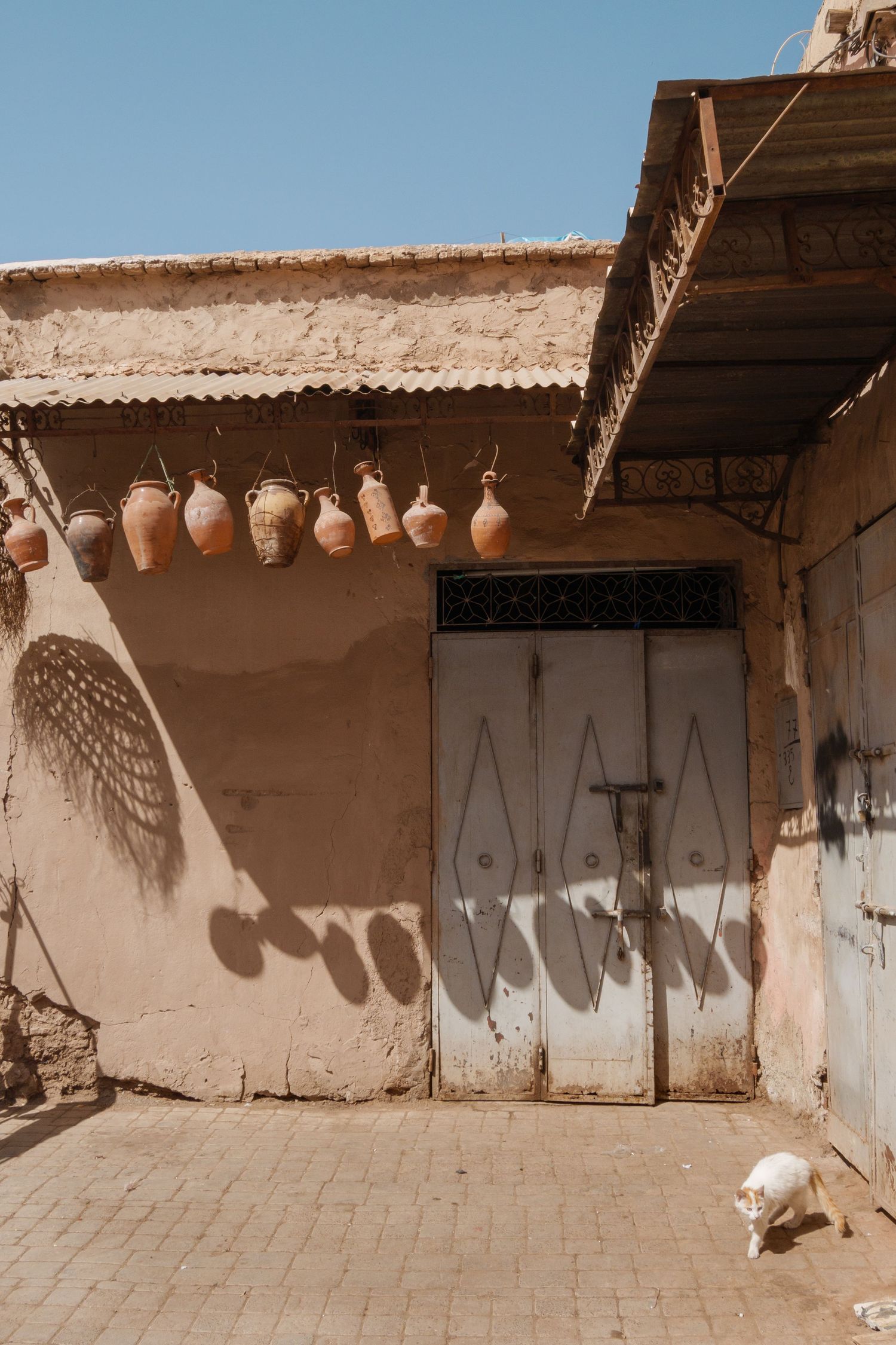 Traditional Moroccan clay pots hanging on a rustic adobe wall beside a white door in sunlight.