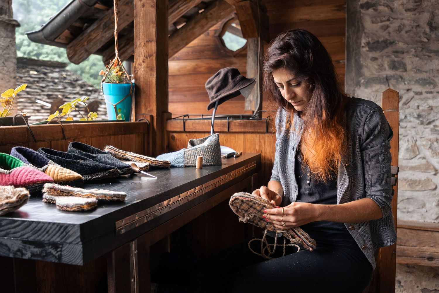 Craftswoman hand-stitching an espadrille shoe sole in a rustic wooden workshop with colorful rope spools.