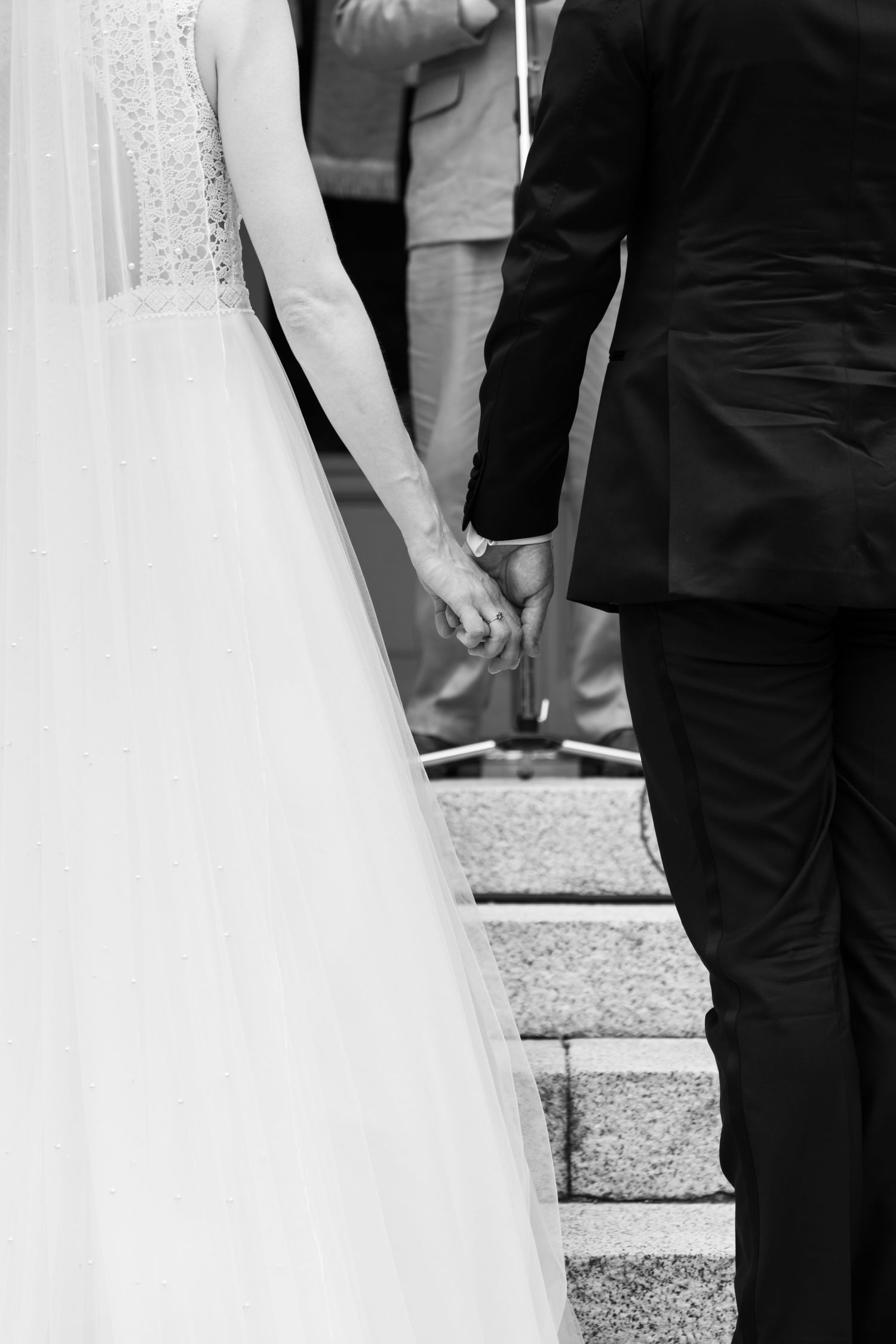 Black and white photo of bride and groom holding hands while descending stone steps after ceremony.