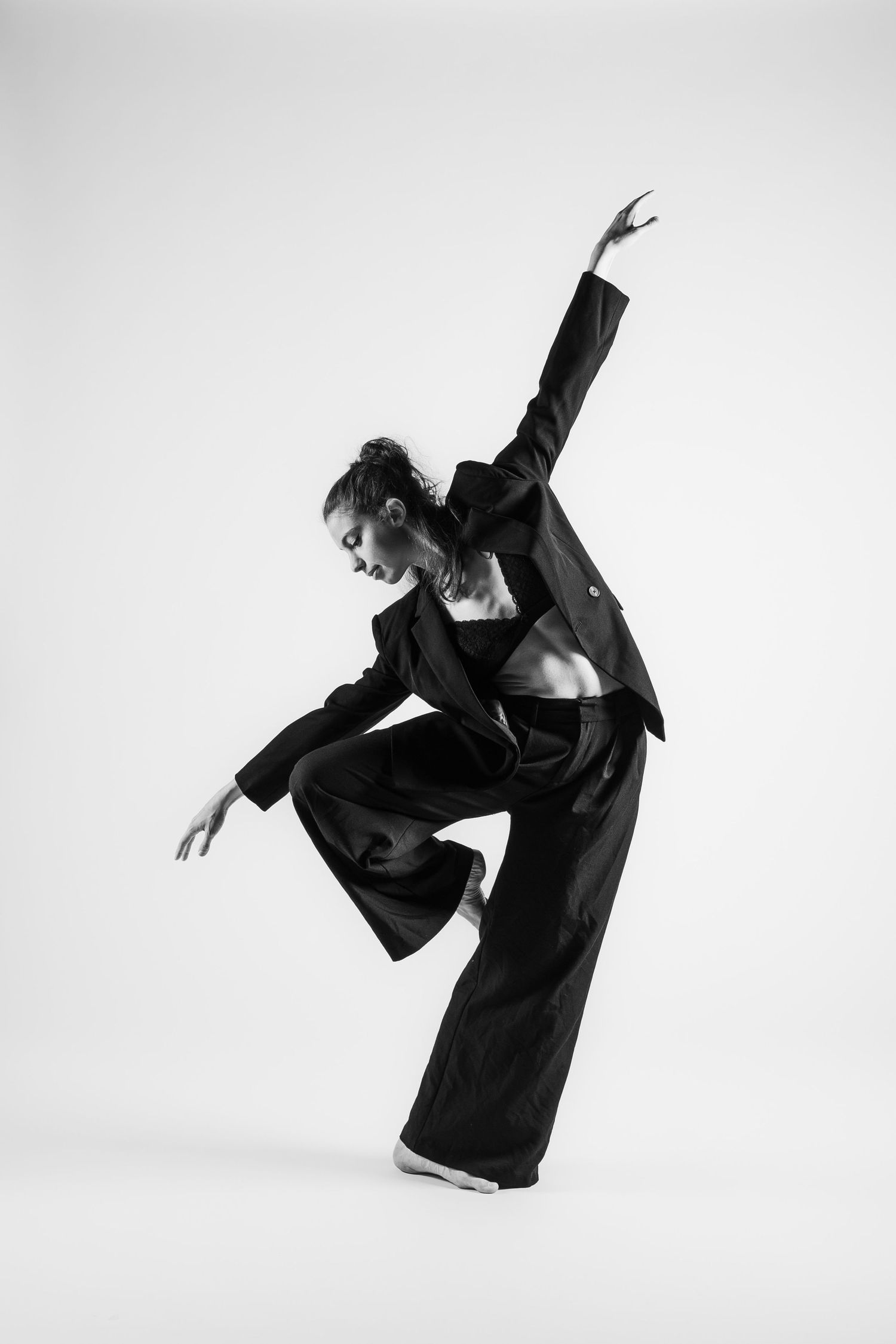 Black and white photo of a contemporary dancer in suit performing a dynamic leaning pose.