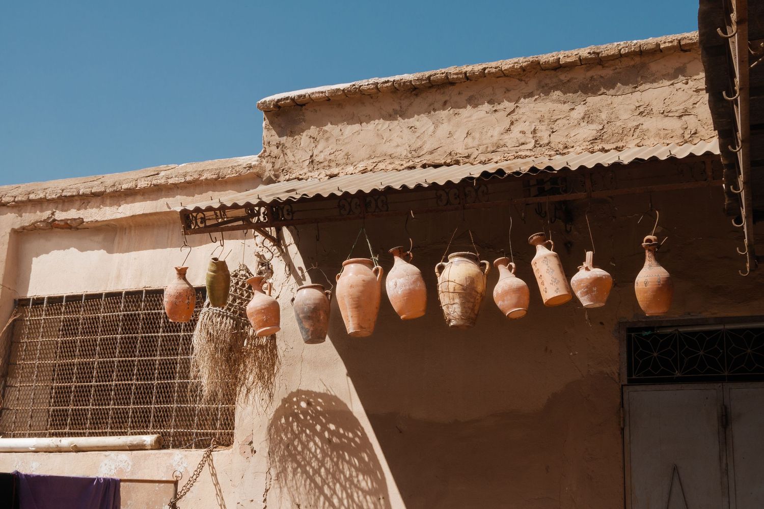 Traditional clay pottery jugs hanging on display outside a rustic desert building.