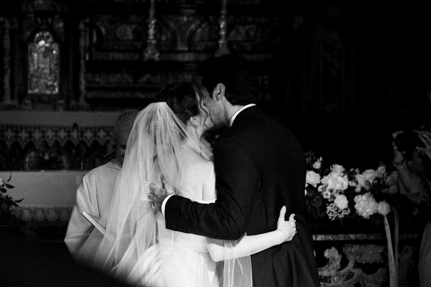 Black and white photo of bride and groom sharing first kiss at the altar during wedding ceremony.
