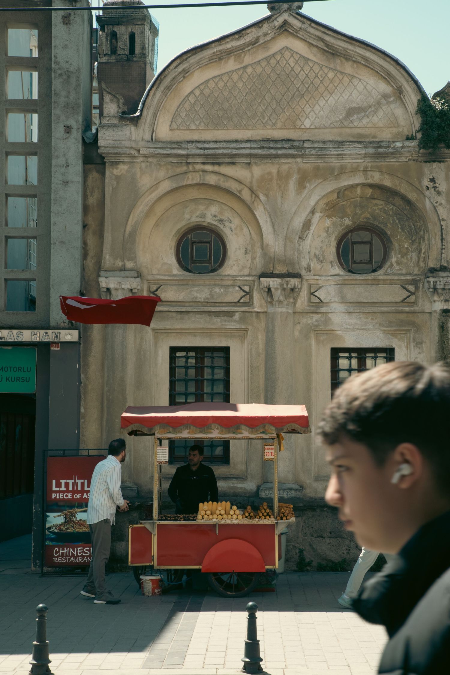 A street food cart vendor selling corn in front of a historic Ottoman building in Istanbul, Turkey.