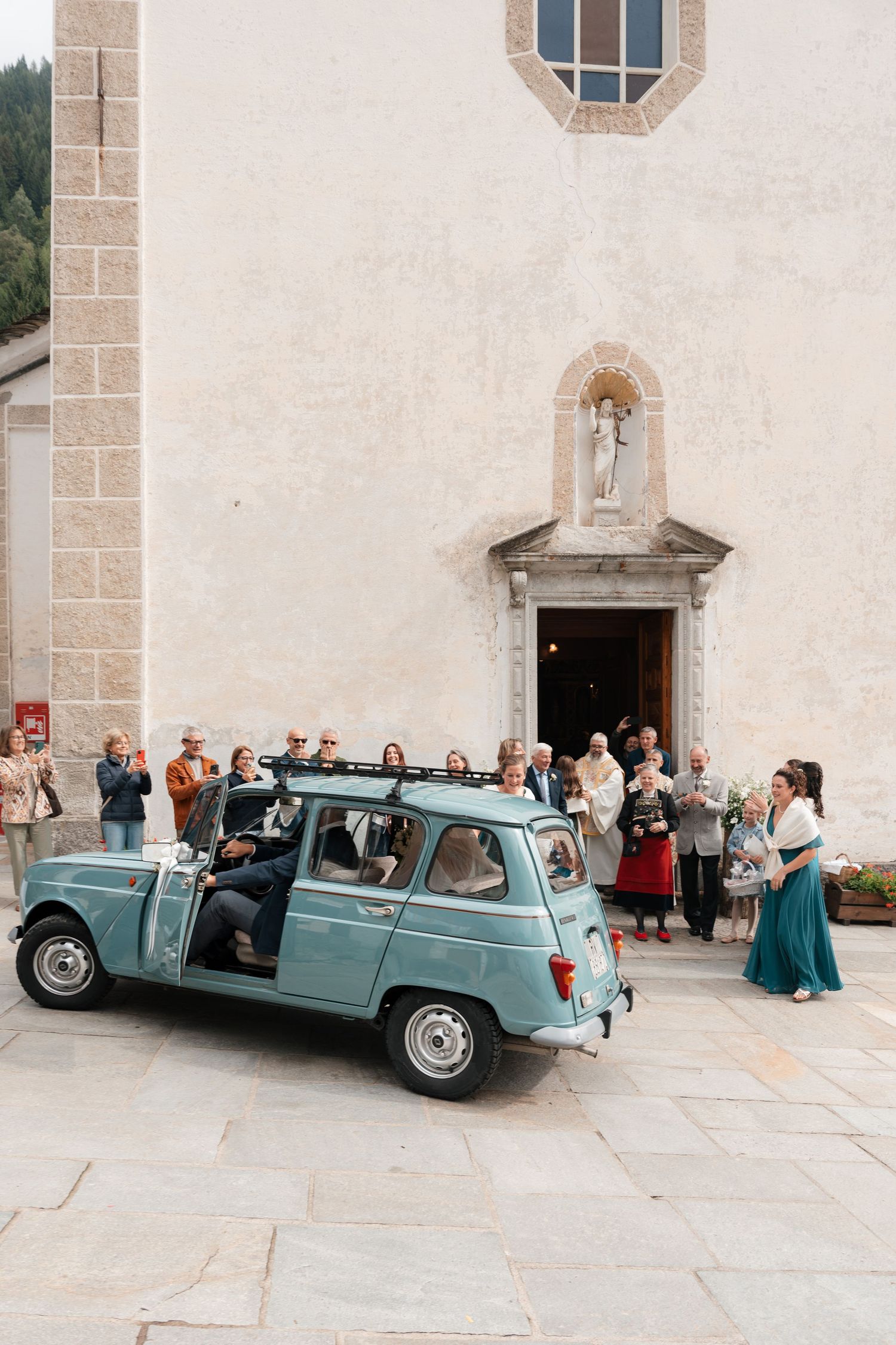 Vintage light blue car parked outside a historic church after a wedding ceremony.