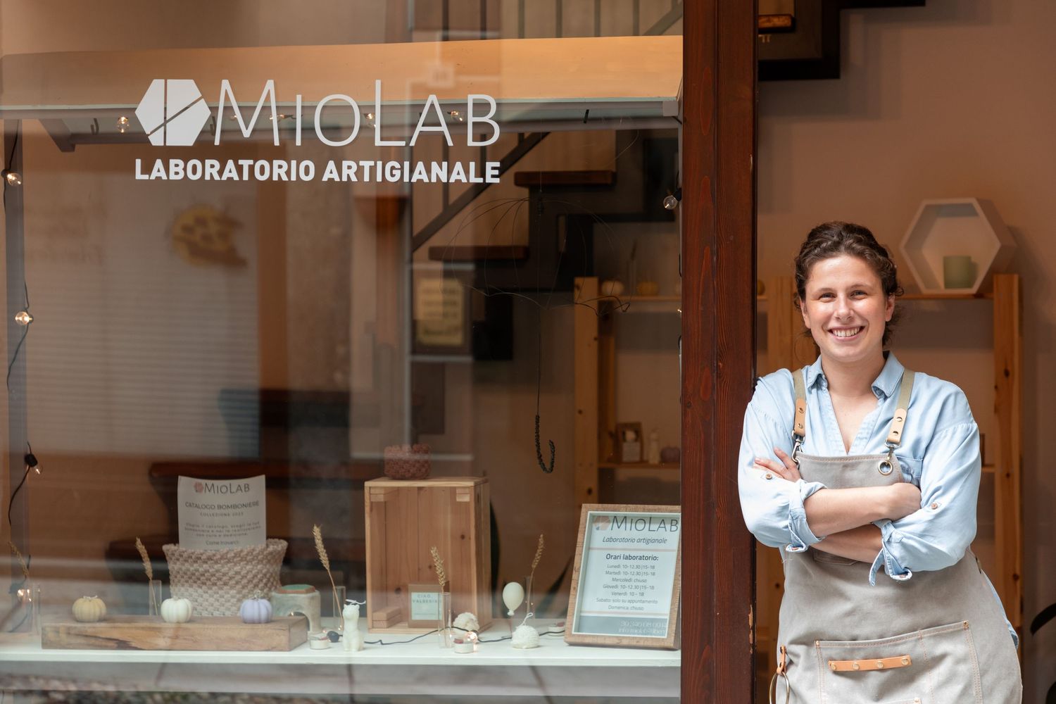 Smiling woman in apron standing confidently outside MioLab artisan workshop storefront.