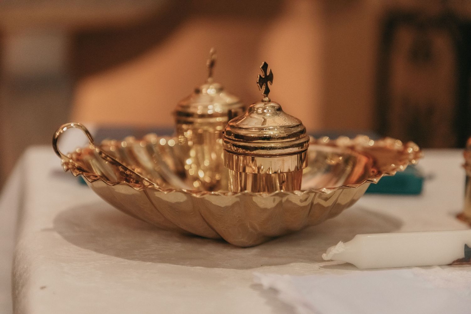 Ornate golden baptismal oil vessels on a decorative shell-shaped tray on a white altar cloth.