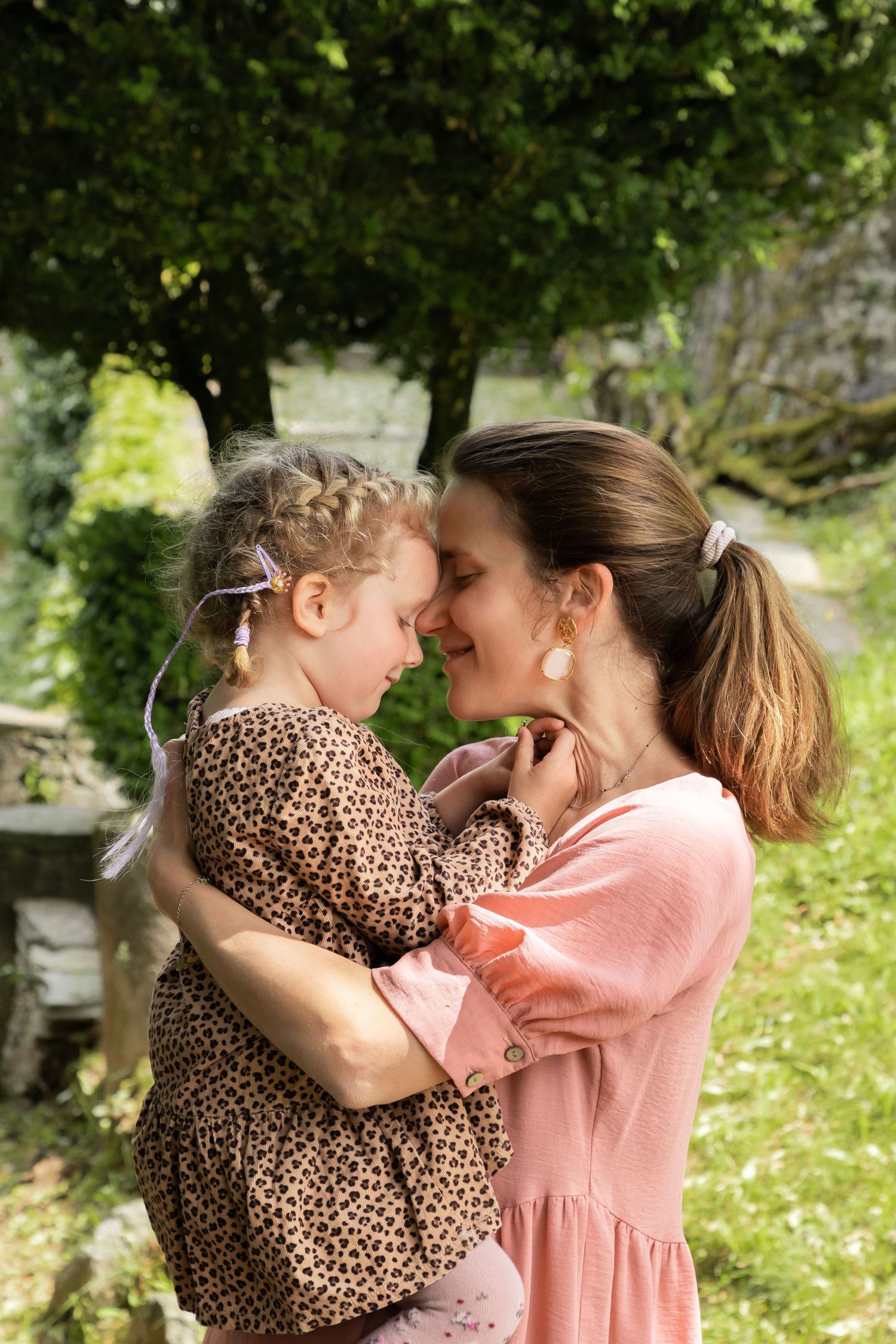 Mother and daughter touching foreheads affectionately in sunny green garden.