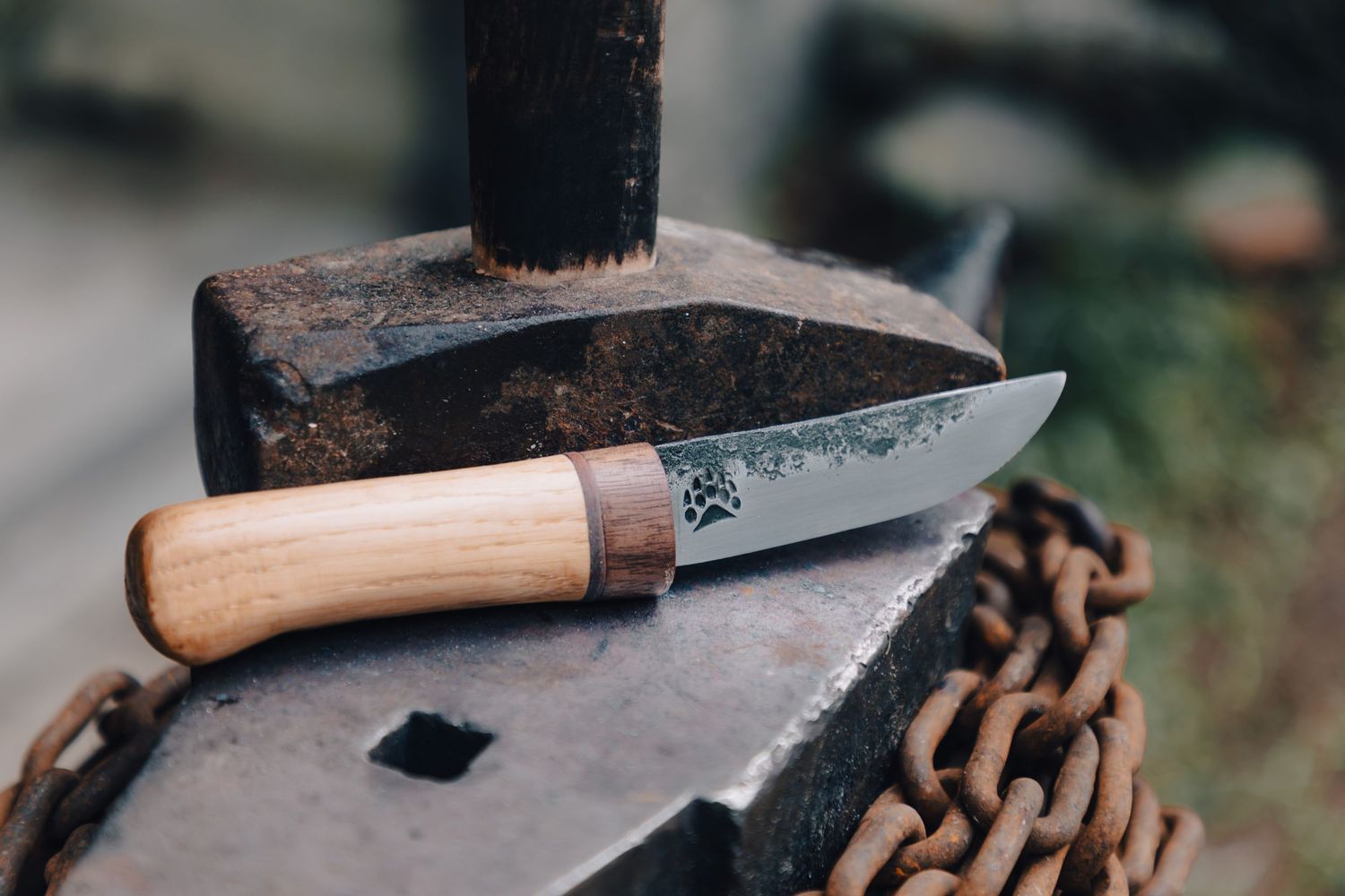 Handcrafted hunting knife with wooden handle resting on rustic anvil with chain nearby.