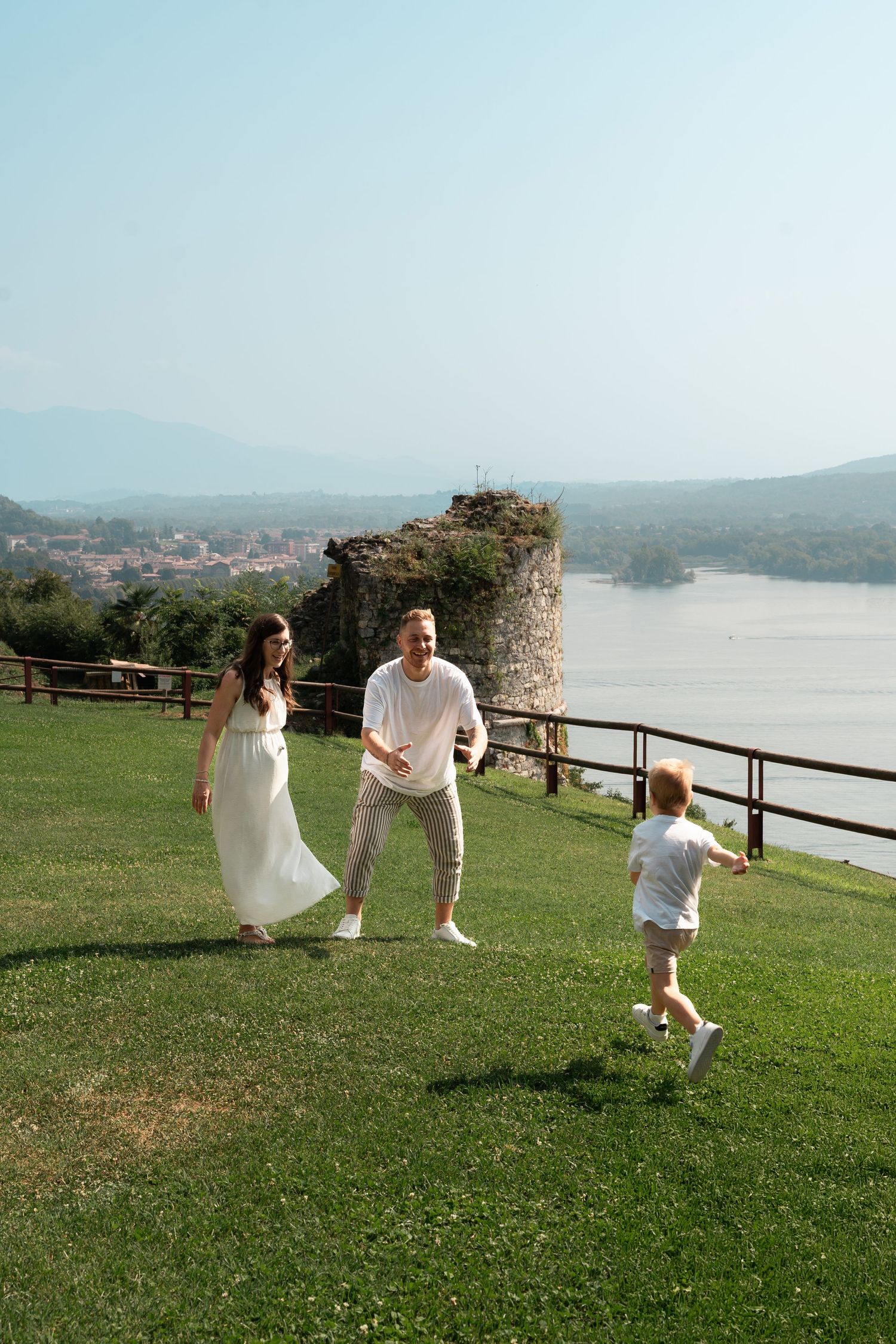 Family playing on green lawn with river and ruins backdrop on sunny day.