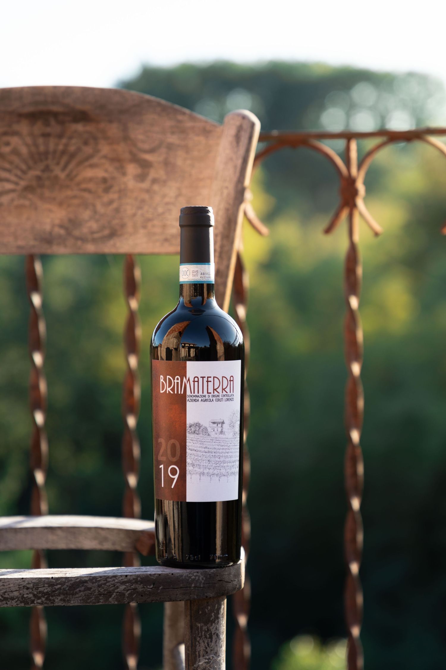 A bottle of Bramaterra 2019 red wine resting on a rustic wooden chair outdoors.