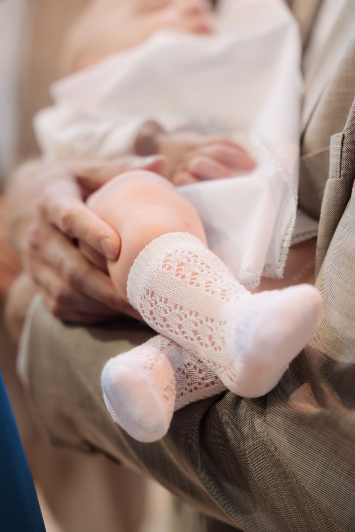 Close-up of a newborn baby wearing white lace socks cradled in arms during a christening ceremony.