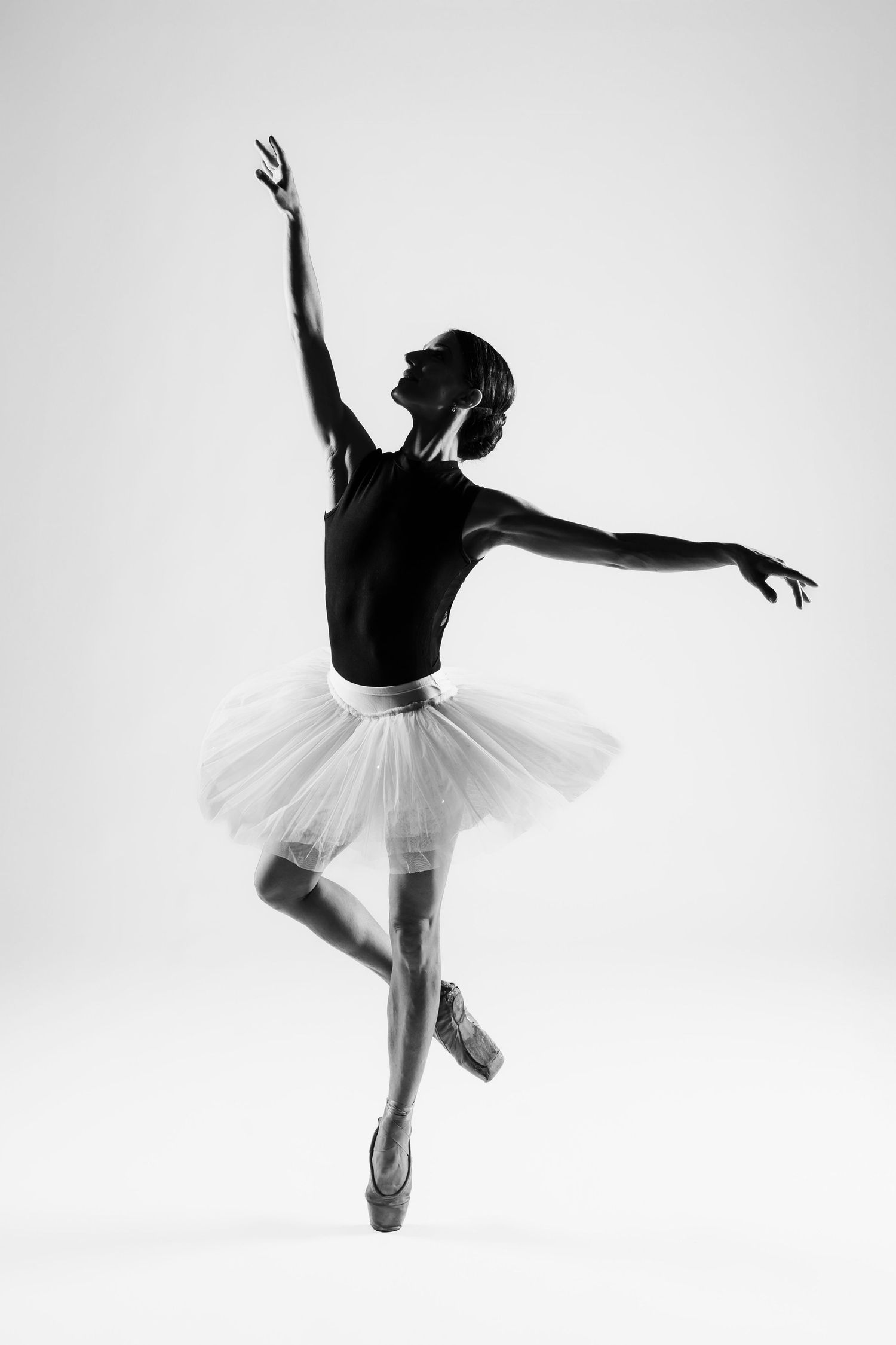 Black and white photo of a ballerina in white tutu performing a classic ballet pose on pointe.