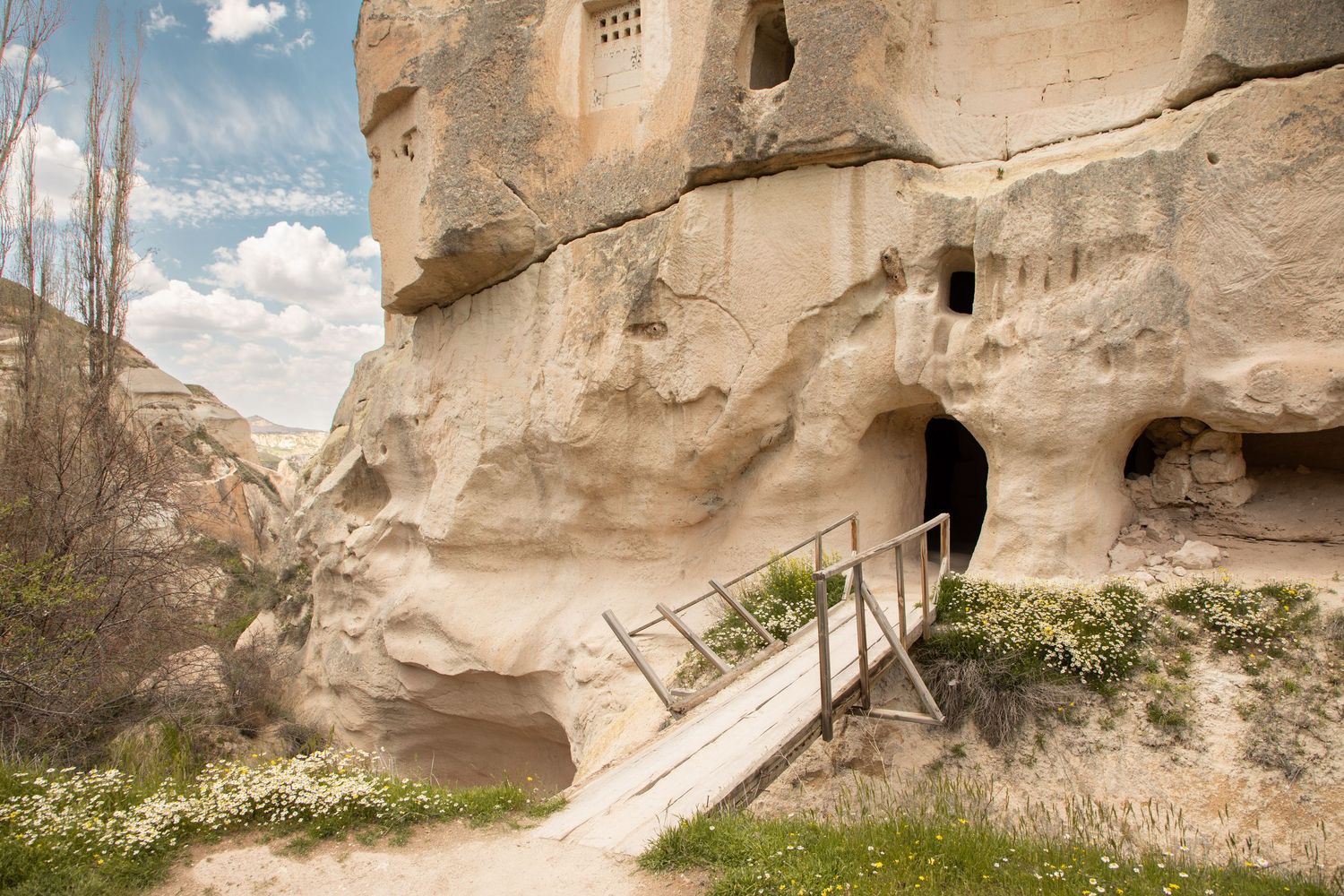 Ancient cave dwelling entrance with wooden ramp and railings carved into soft volcanic rock in Cappadocia.