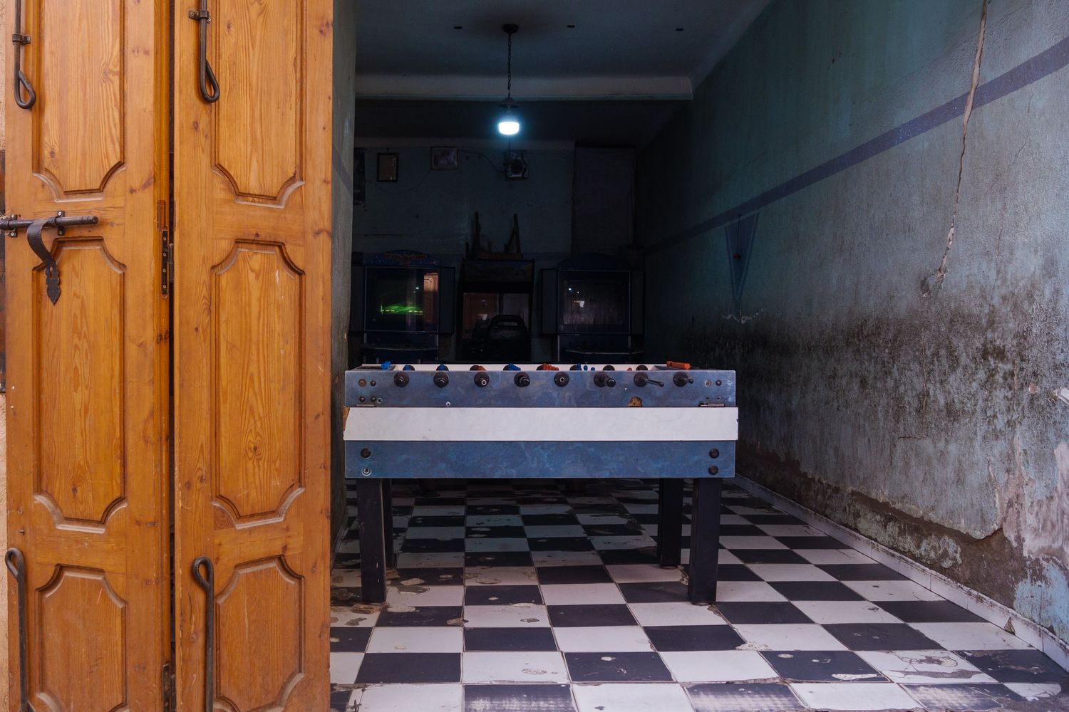 Vintage foosball table on a checkered floor beside ornate wooden doors in a dimly lit Moroccan room.