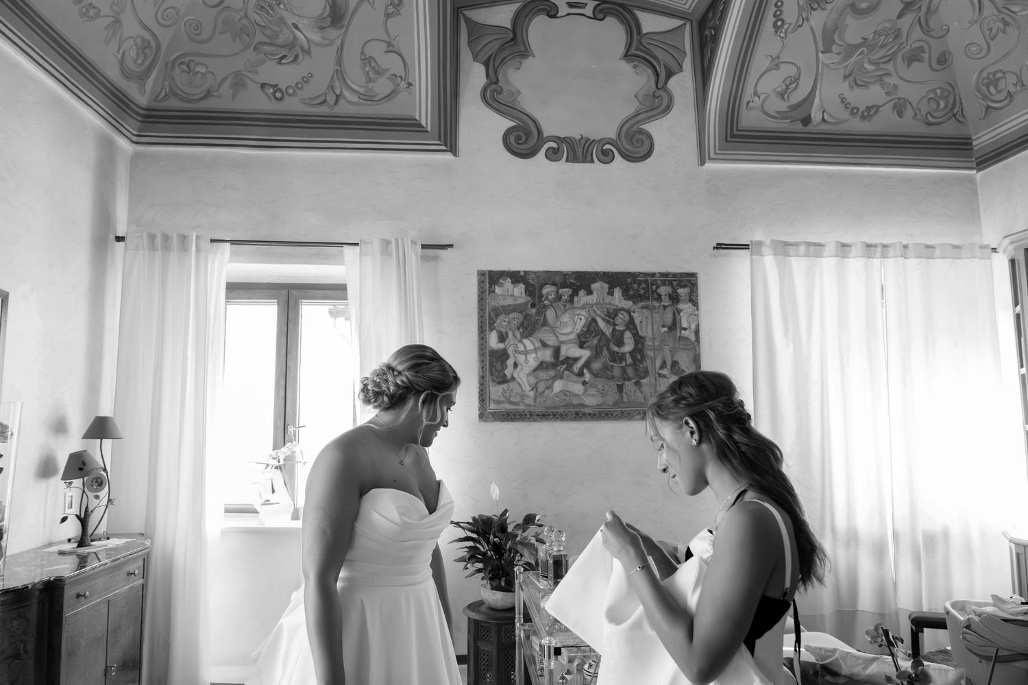Black and white photo of bride and bridesmaid in elegant frescoed Italian villa room.