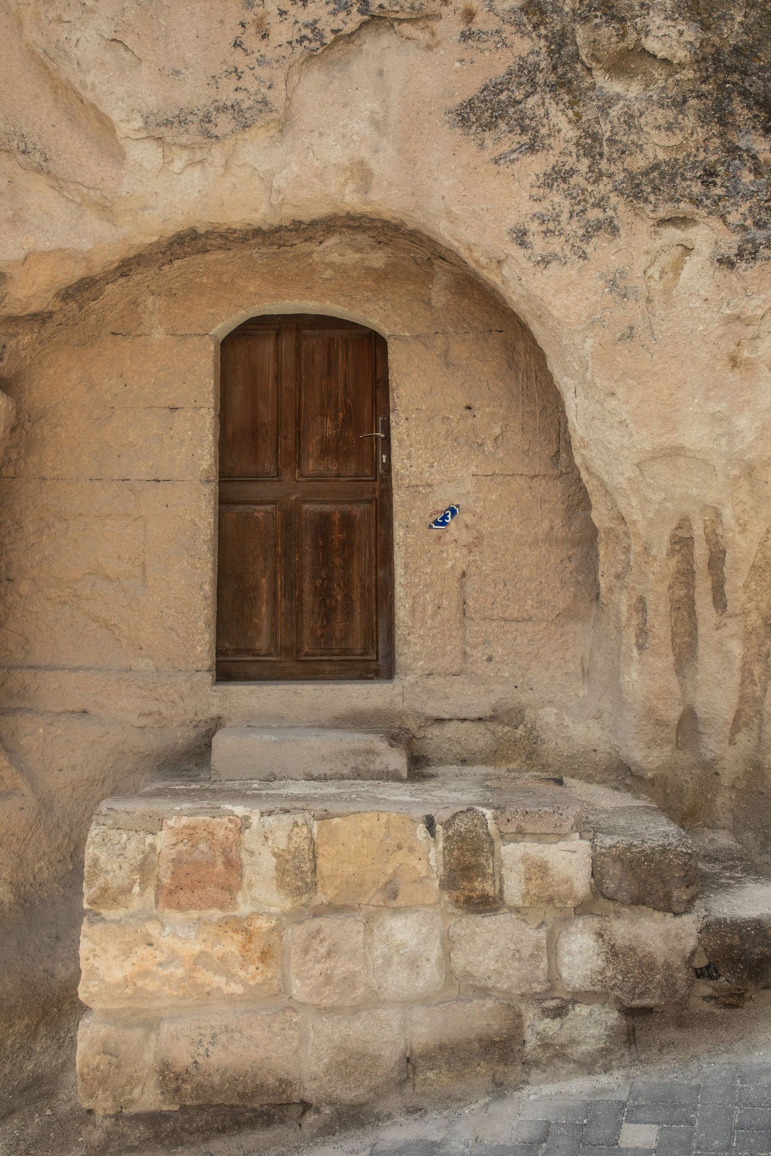 Rustic wooden arched door set into a carved cave rock facade with stone steps leading up.