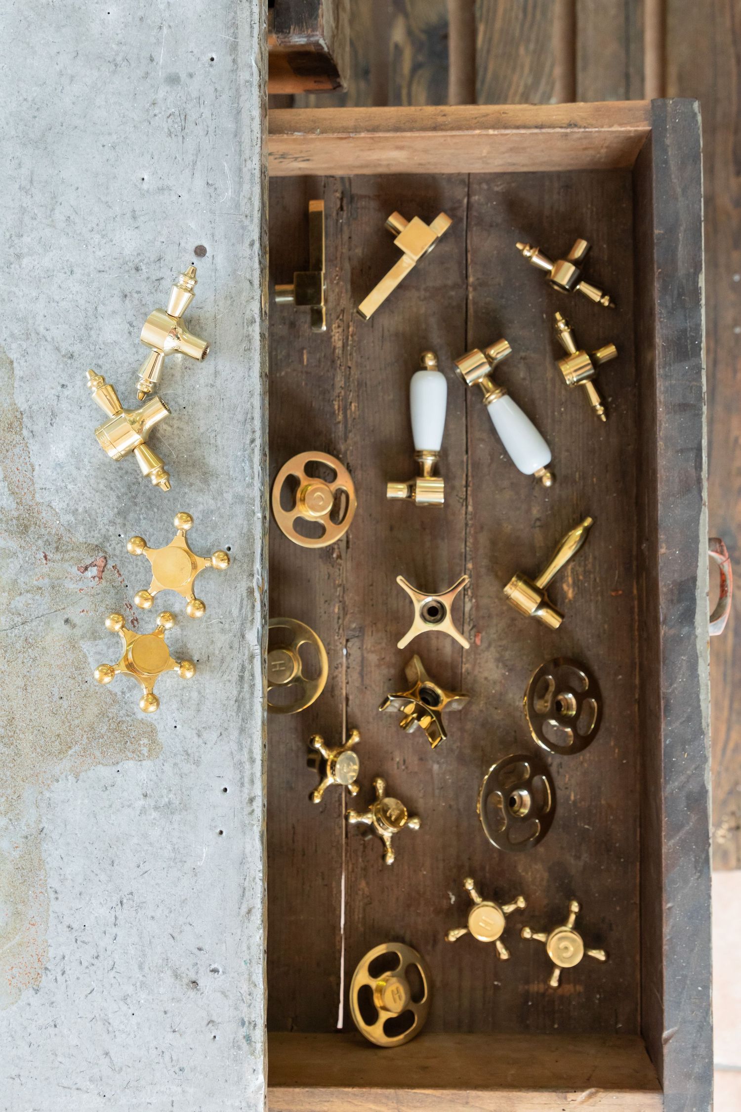 A wooden drawer displaying a collection of antique brass faucet handles and valves.