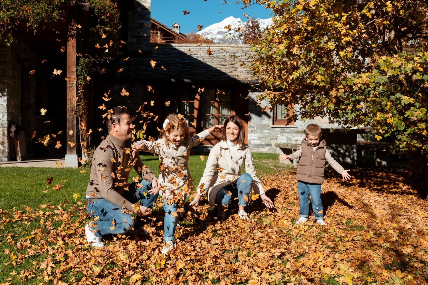 Happy family playing and tossing autumn leaves together in yard during colorful fall season outdoors.