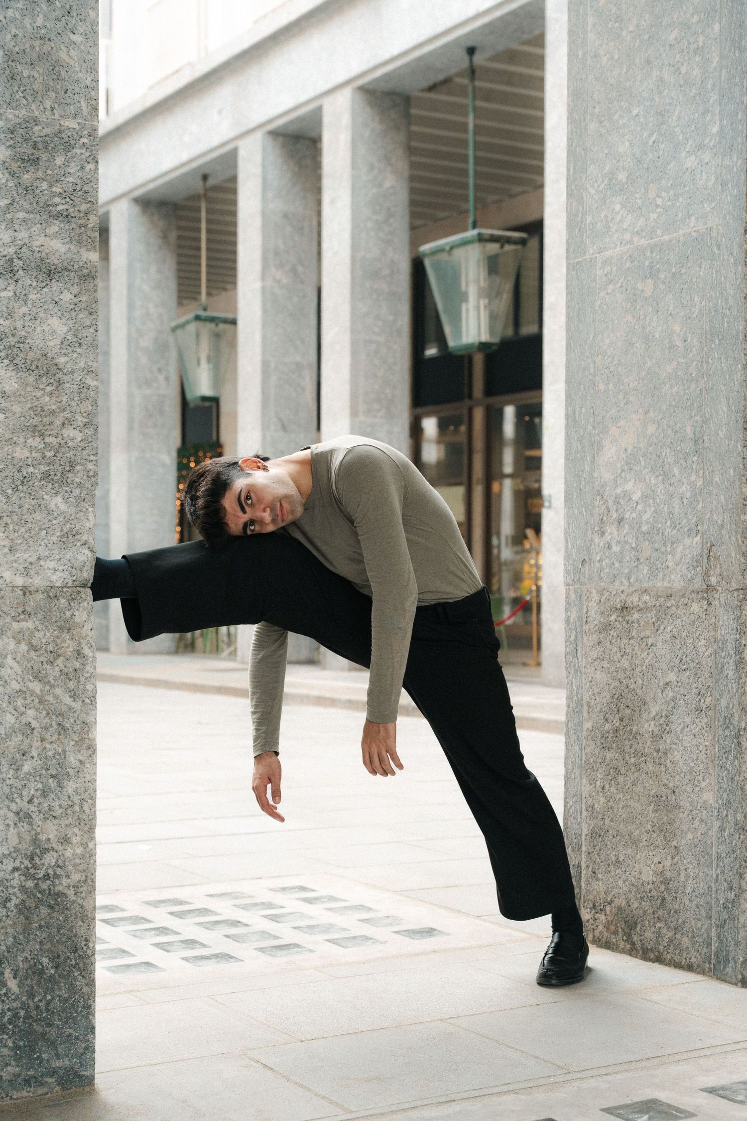 Male contemporary dancer in grey top bending dramatically between modern concrete pillars.