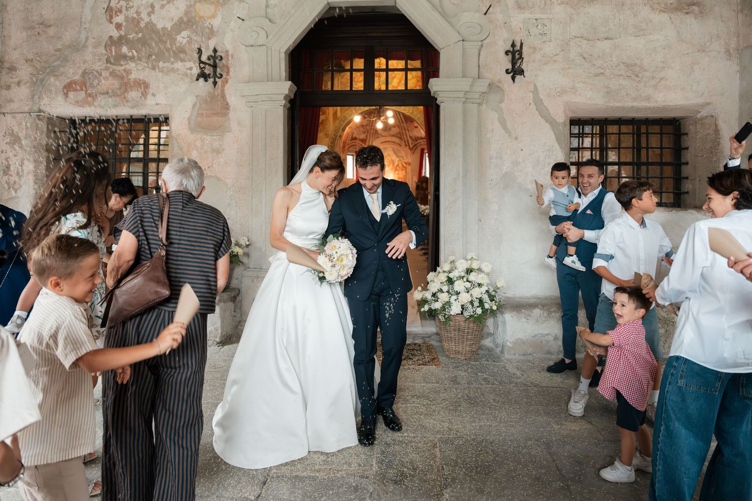 Newlyweds exit historic stone church doorway as guests celebrate with confetti and cheers.