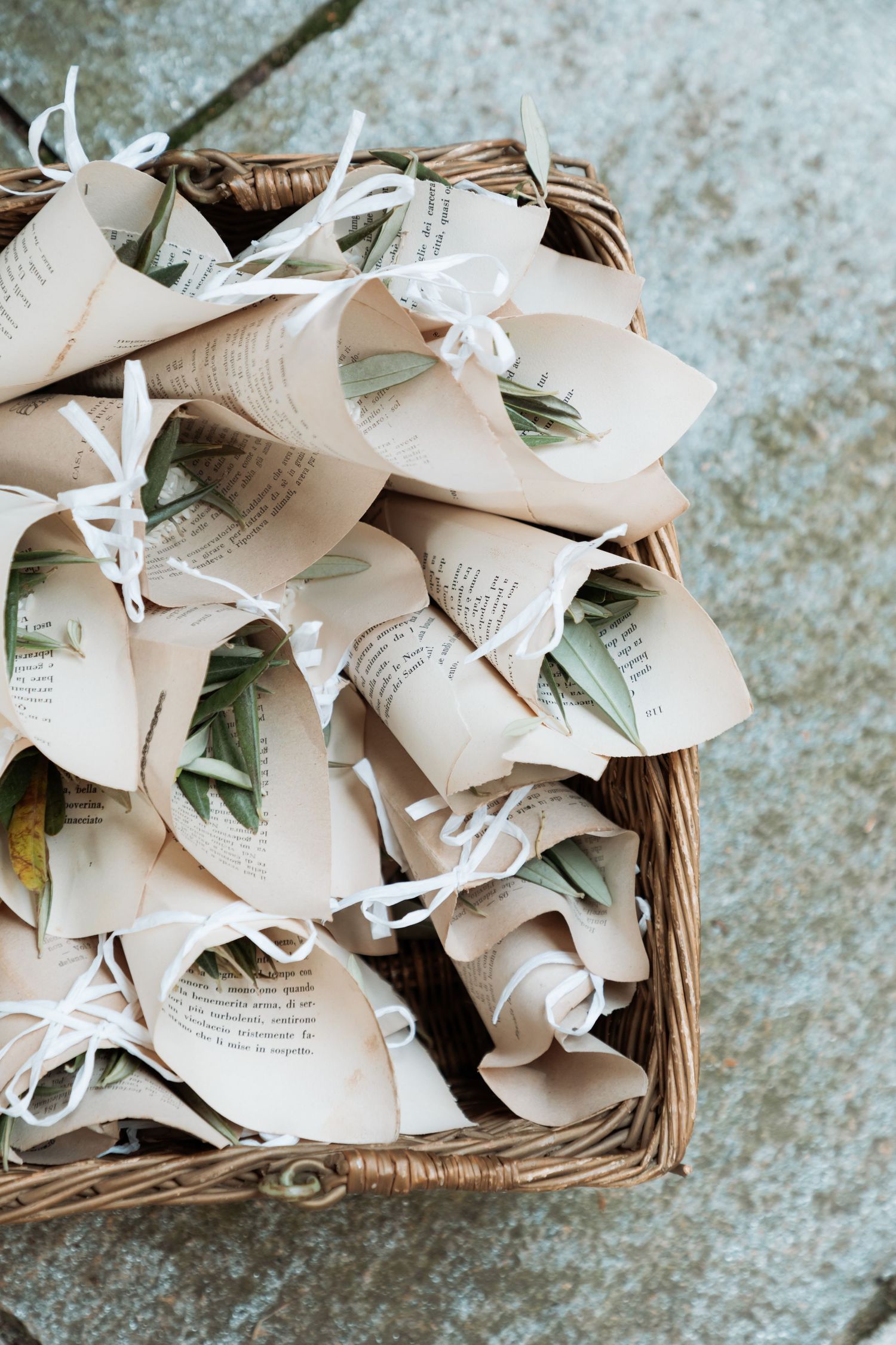 Rustic wicker basket filled with paper cone favors made from book pages tied with white ribbons.